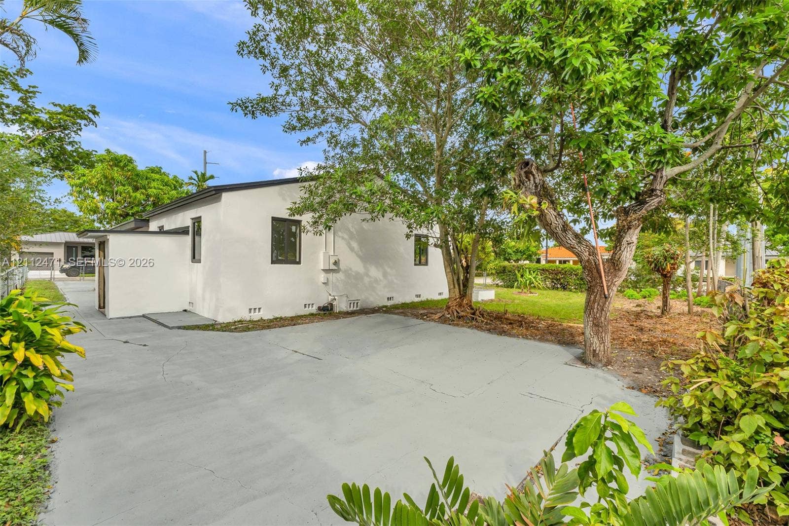 Stucco exterior with a paved driveway, mature trees, and landscaping