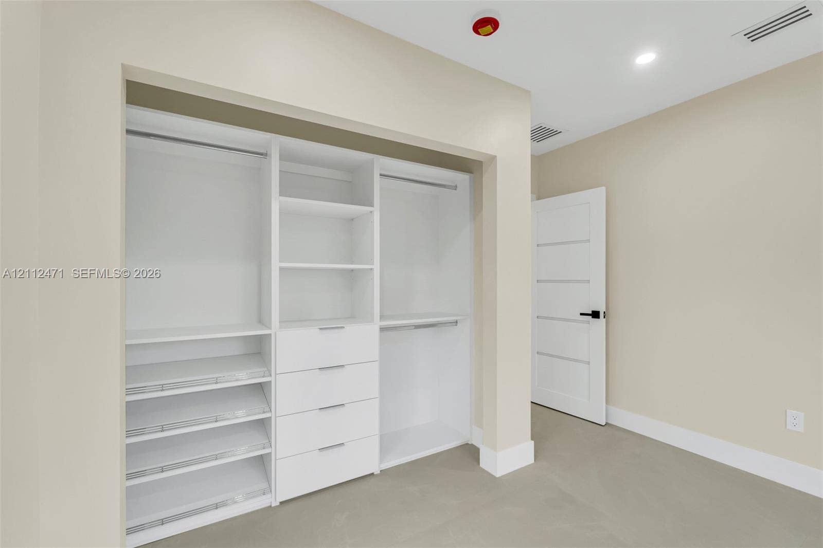 Custom white built-in cabinetry featuring tiered shelving, integrated storage drawers, and hanging rods, complemented by a five-panel interior door with matte black hardware