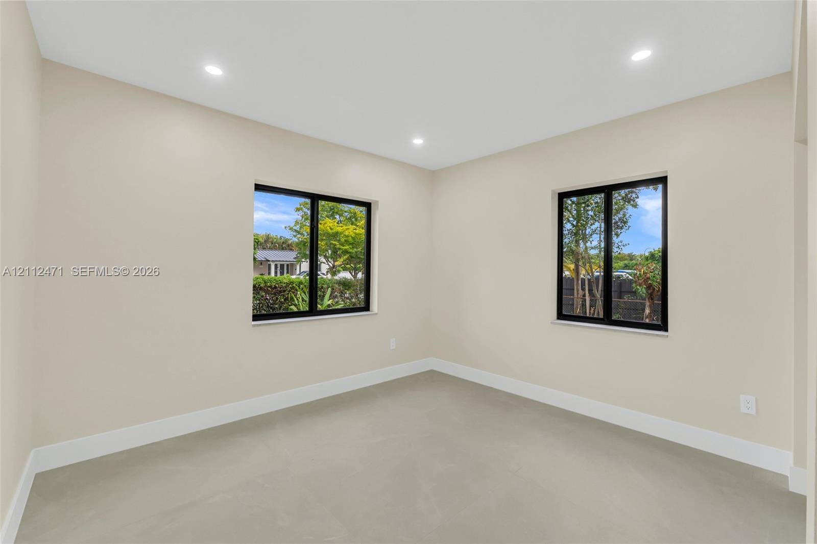 Interior space featuring neutral-toned walls, recessed lighting, dual windows with dark frames, and uniform hard-surface flooring