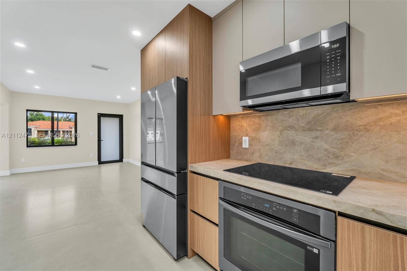 Modern kitchen featuring slab-front cabinetry, stone-patterned backsplash, stainless steel appliances, and integrated under-cabinet lighting