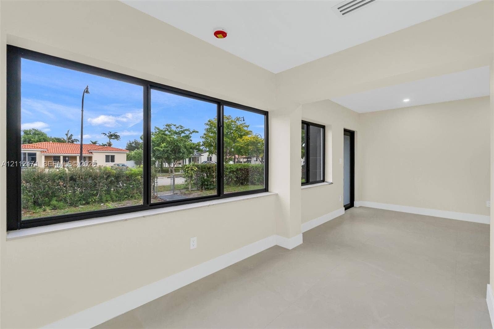 Neutral-toned interior space featuring large, black-framed windows, recessed lighting, and uniform tile flooring