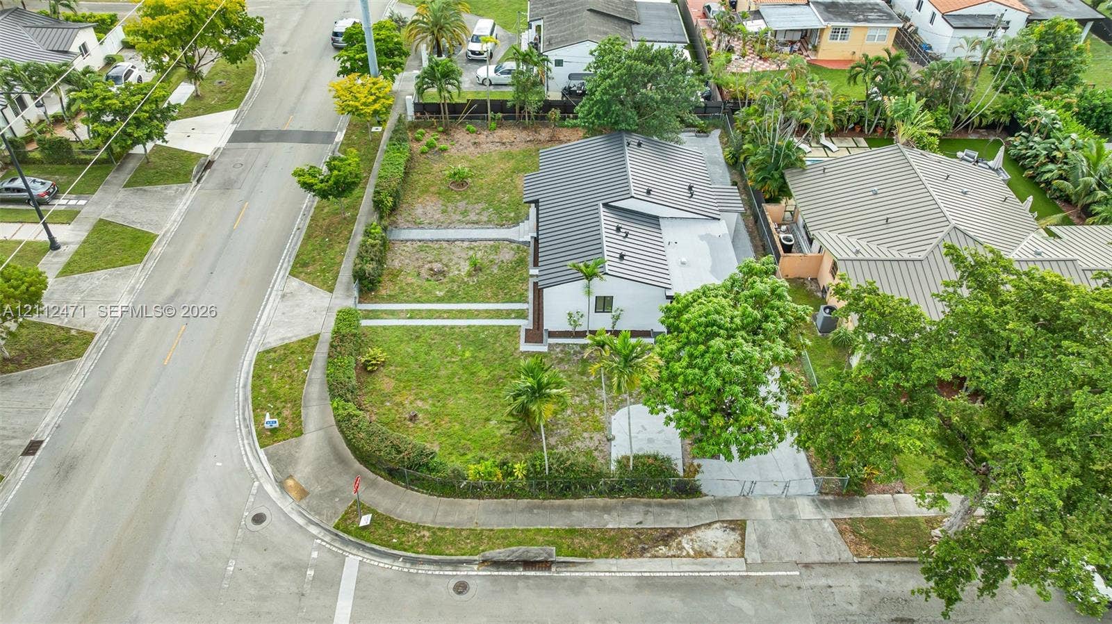 Corner lot residence featuring a standing seam metal roof, paved driveway, and established perimeter landscaping