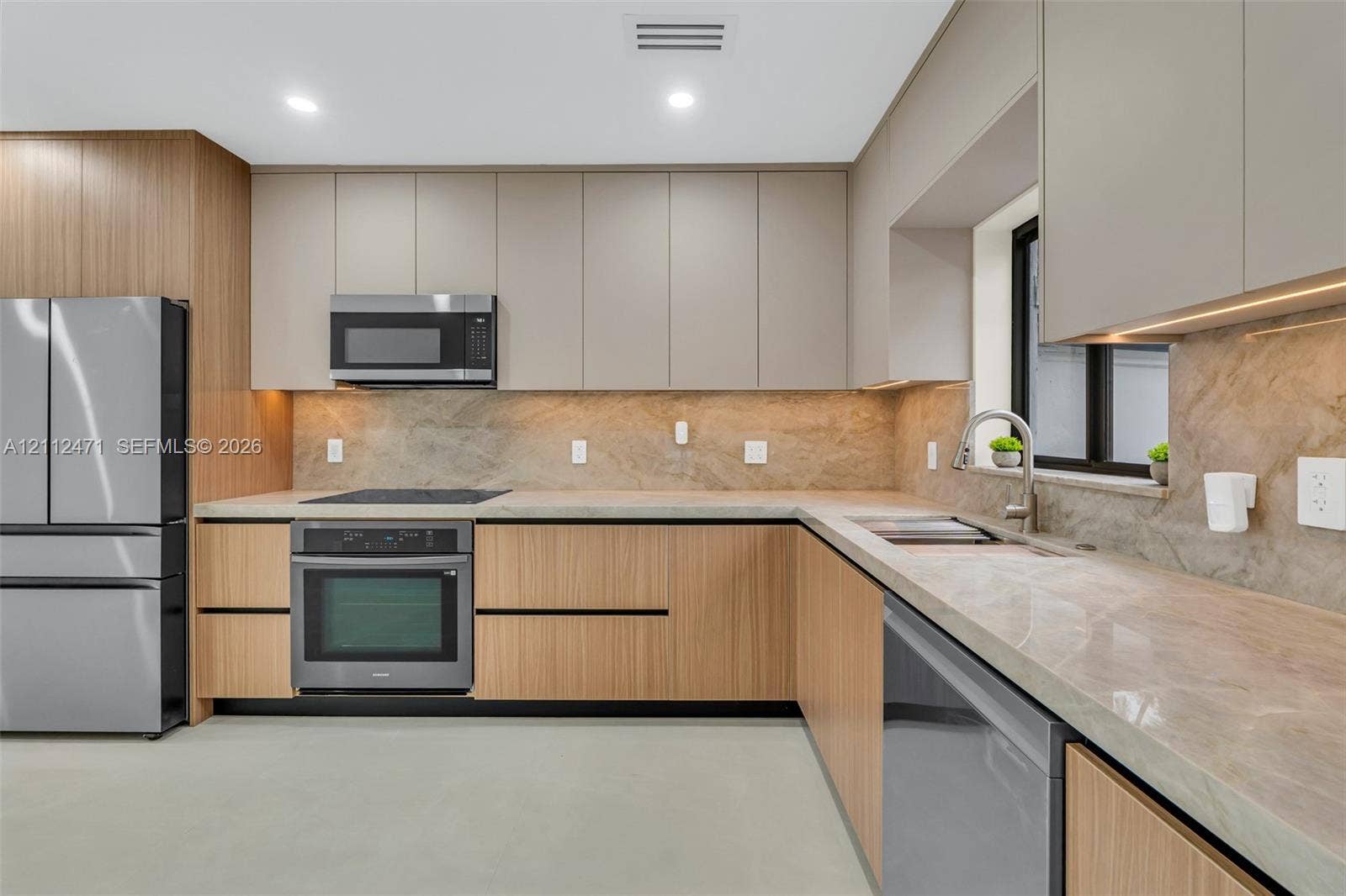 Kitchen featuring two-tone flat-panel cabinetry, stone-finish countertops, full-height stone backsplash, and stainless steel appliances