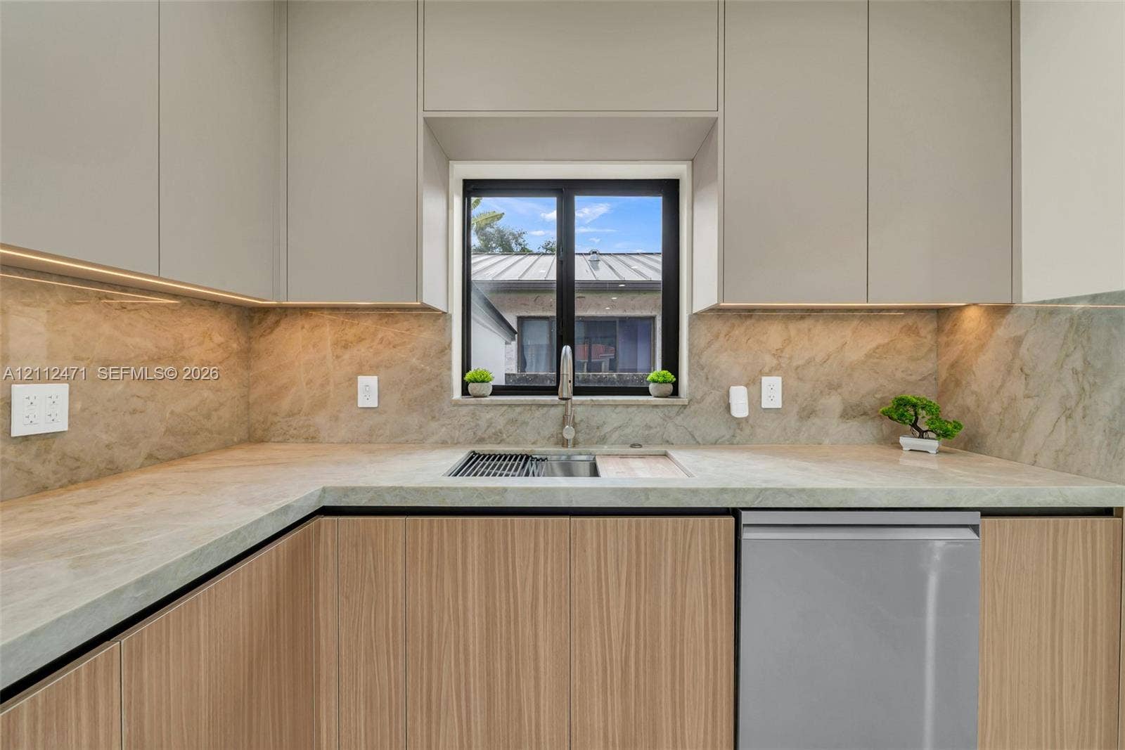 Flat-panel cabinetry with light wood grain finish, integrated stainless steel appliances, stone countertop, full-height stone backsplash, and undermount sink with a pull-down faucet
