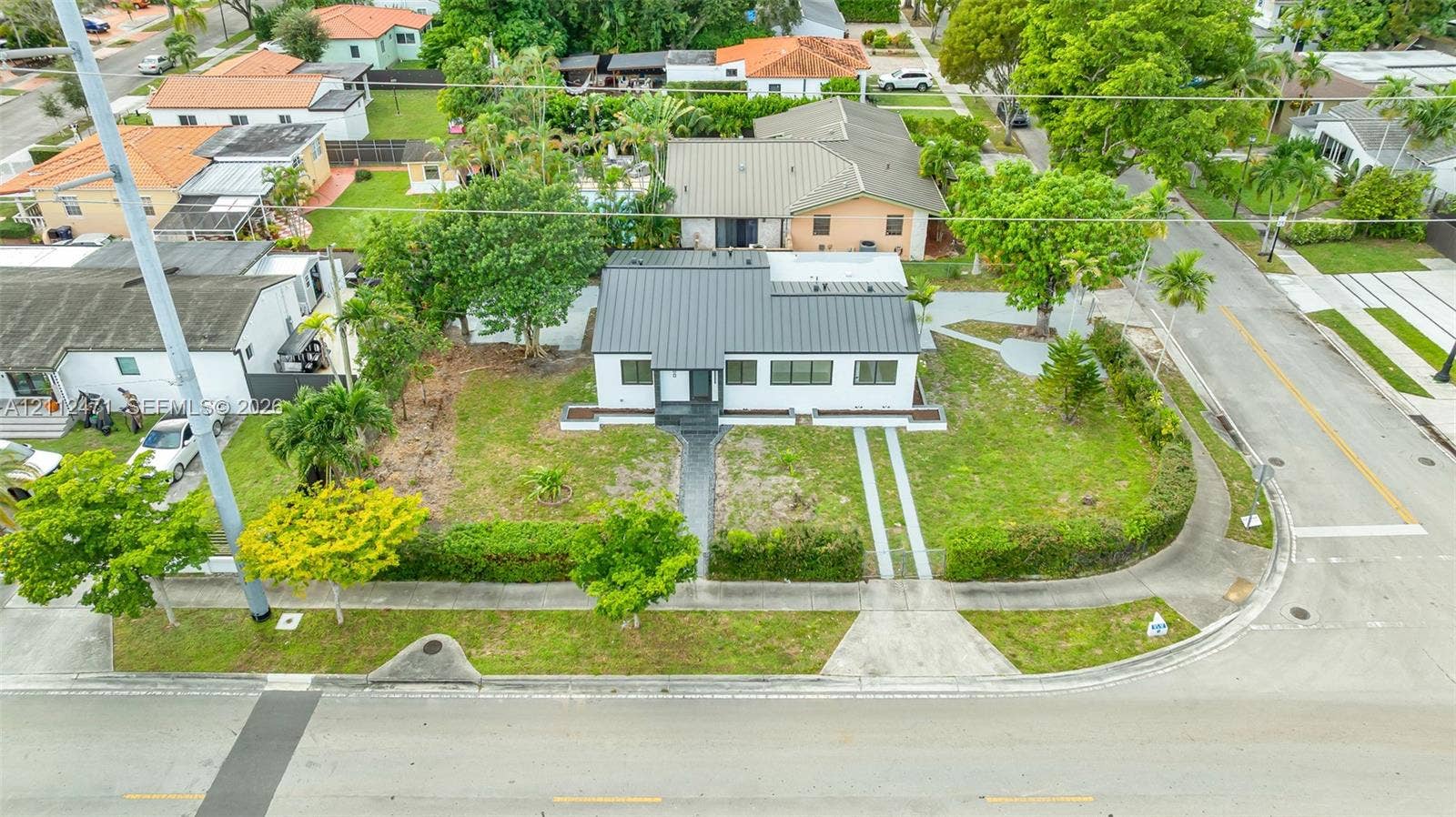 Corner lot residence featuring a standing-seam metal roof, white exterior siding, manicured hedges, and dual concrete driveway strips