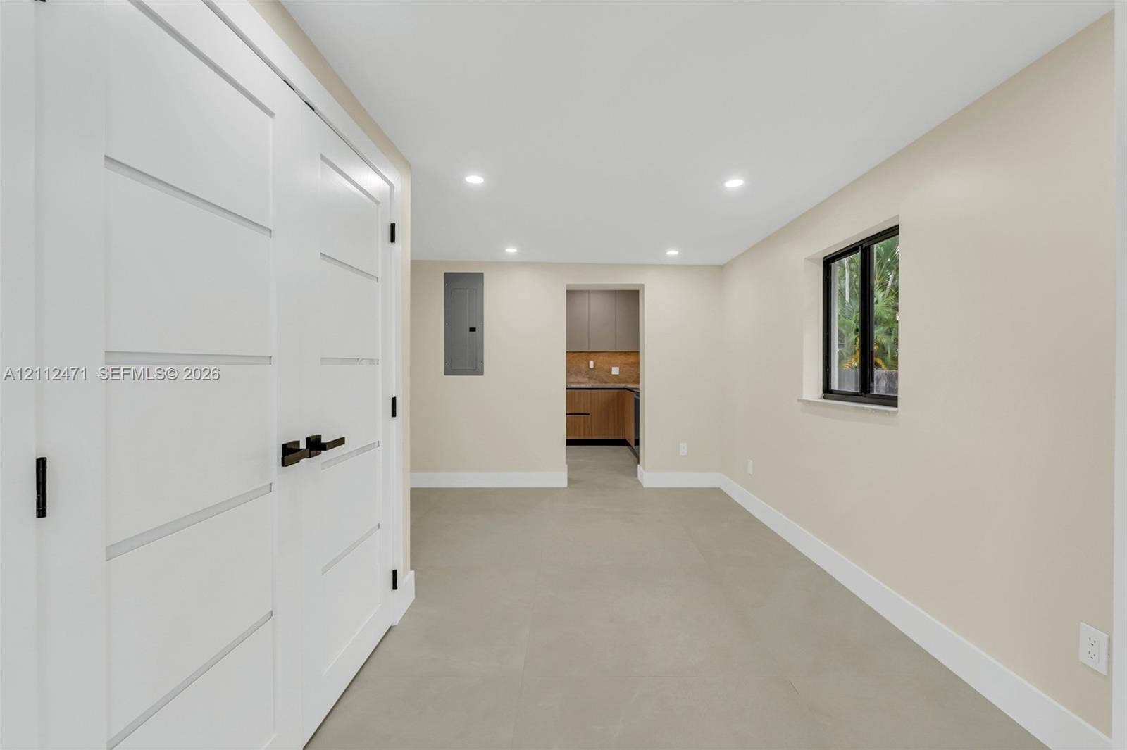 Neutral-toned interior featuring recessed lighting, large-format tile flooring, a window with a dark frame, and white shaker-style double doors with matte black hardware