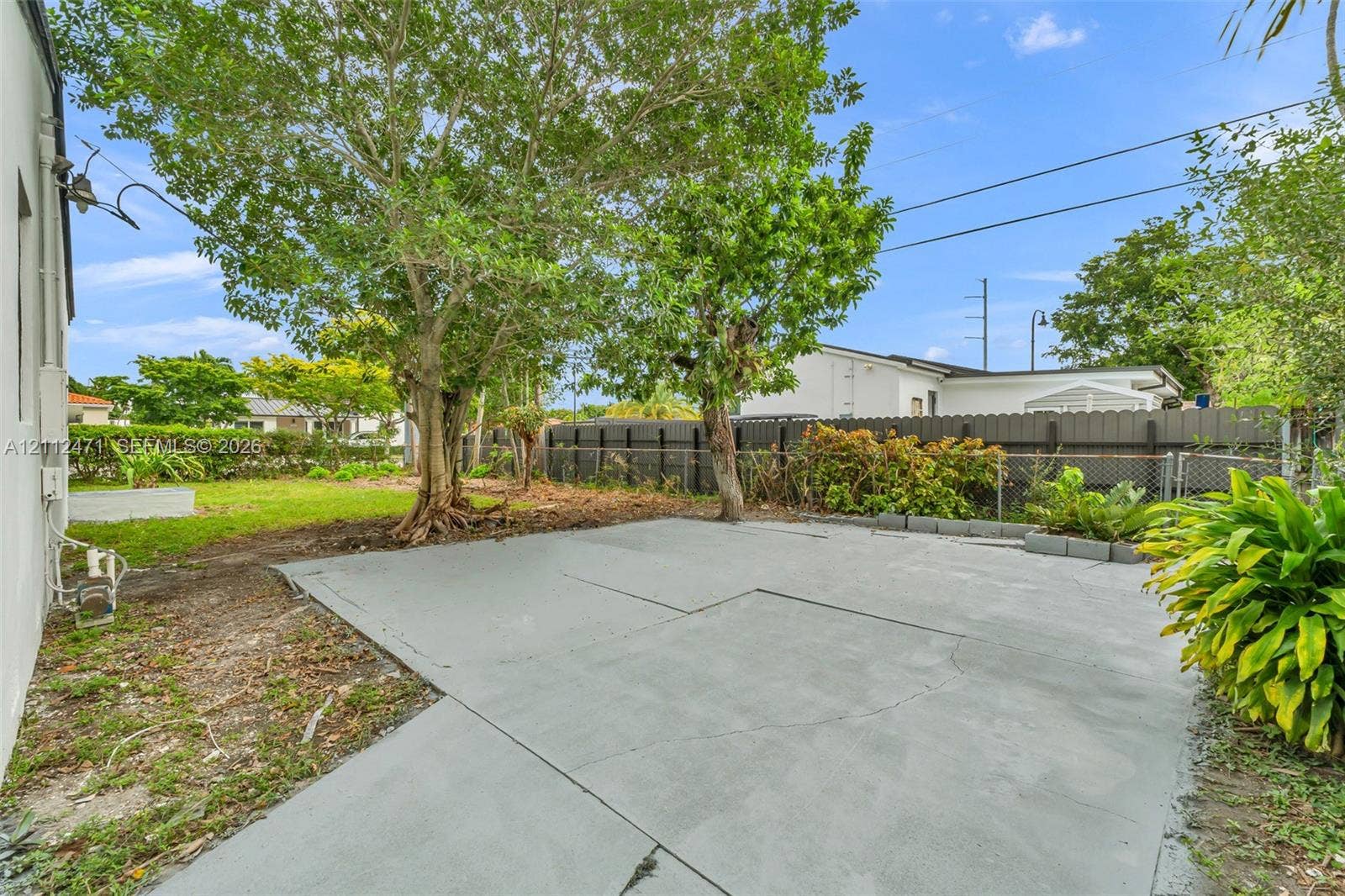 Concrete patio, fenced perimeter, mature trees, and landscaped green space