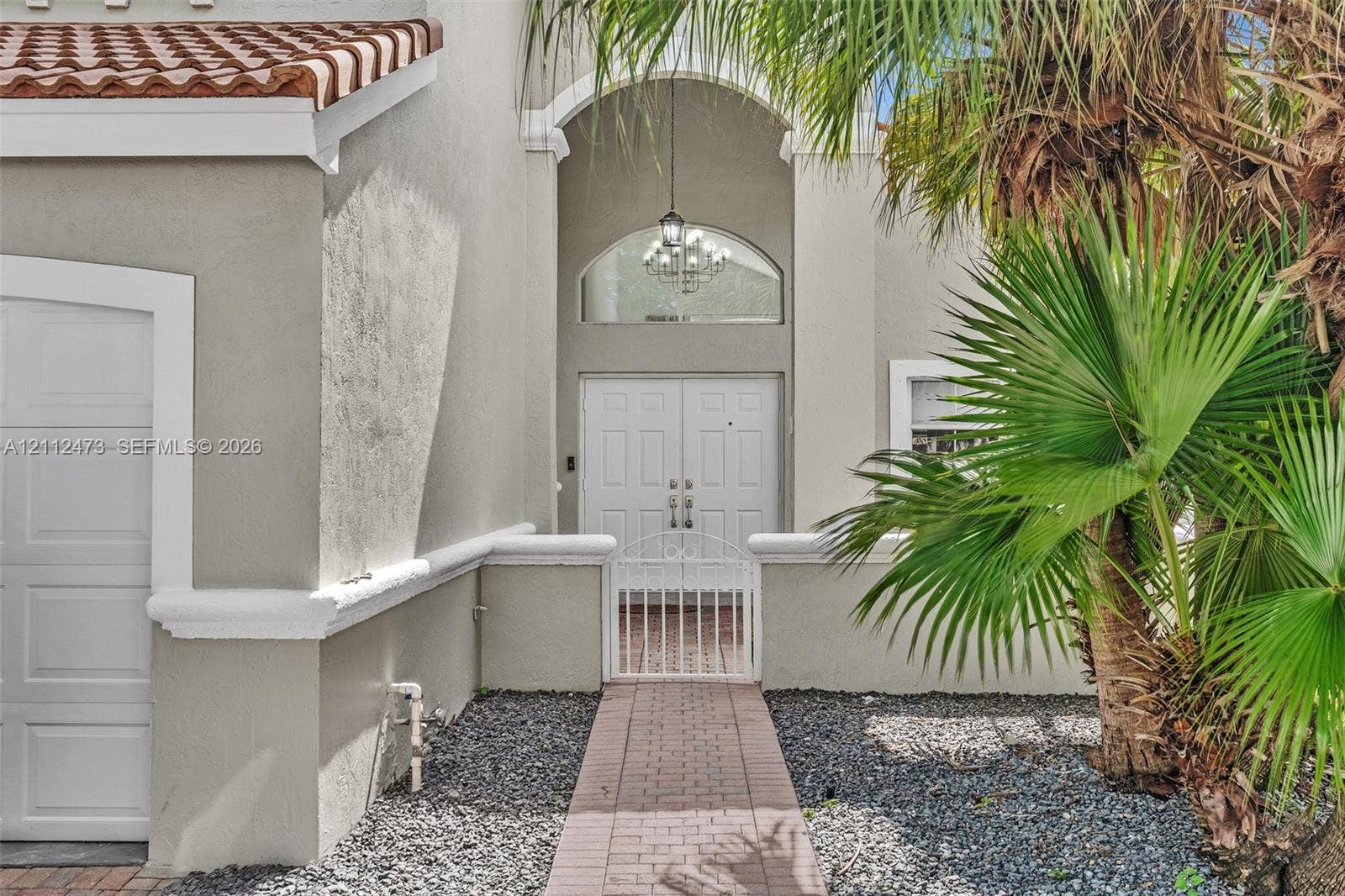 3340 SW 50th Street, Hollywood, Hollywood, FL 33312 Stucco exterior featuring an arched entryway, double-door entrance, red tile roofing, decorative chandelier, and a paved walkway
