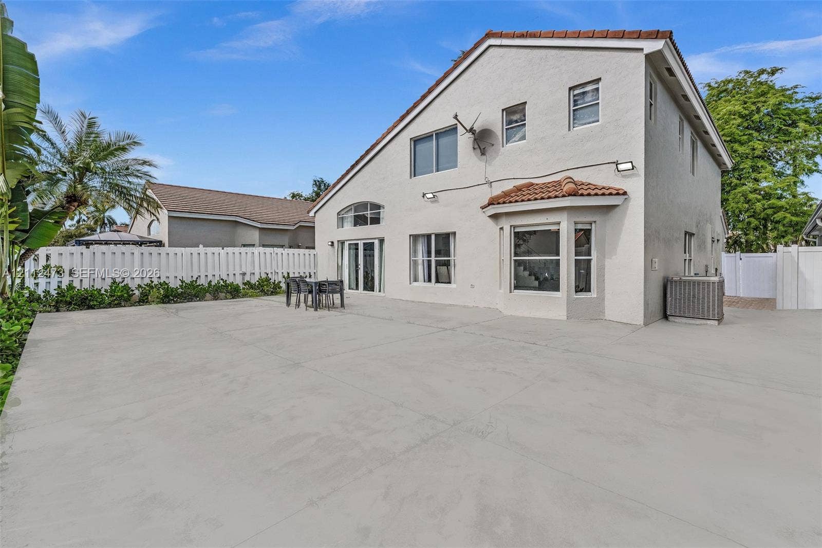 3340 SW 50th Street, Hollywood, Hollywood, FL 33312 Stucco exterior featuring a tile-accented roof, expansive concrete patio, bay window, and white vinyl privacy fencing