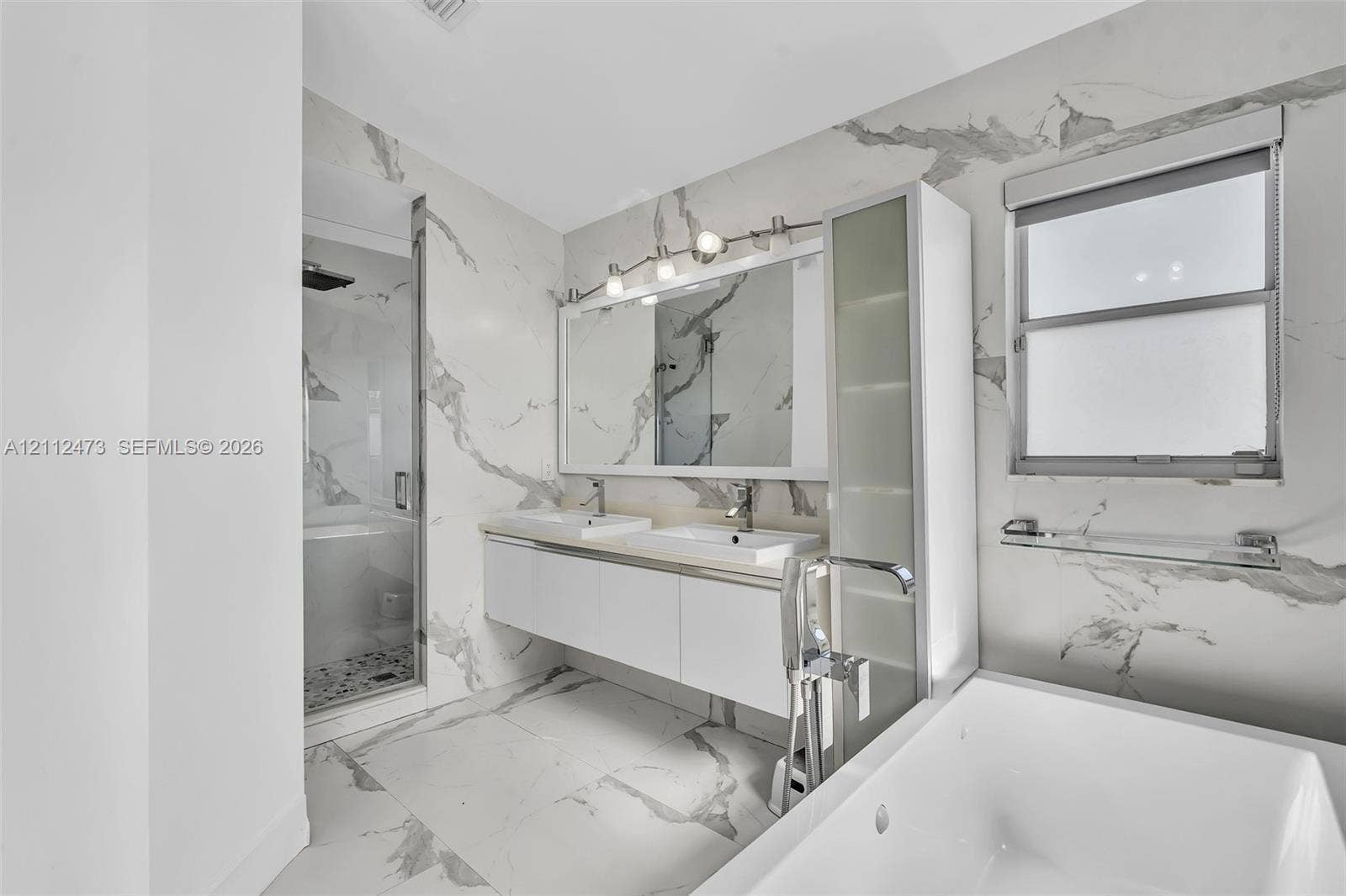 3340 SW 50th Street, Hollywood, Hollywood, FL 33312 Bathroom featuring floor-to-ceiling large-format stone-patterned wall tile, white floating double vanity with integrated sinks, glass-enclosed walk-in shower, soaking tub, and built-in vertical storage cabinet