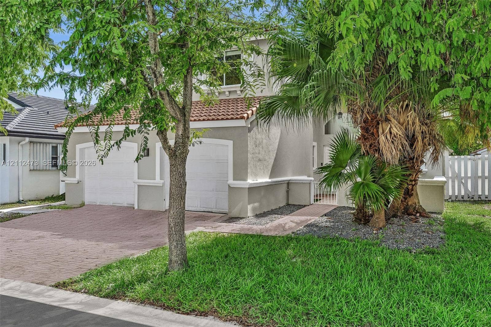 3340 SW 50th Street, Hollywood, Hollywood, FL 33312 Stucco exterior featuring a two-car garage, red clay tile roofing, decorative trim detailing, and a paved brick driveway