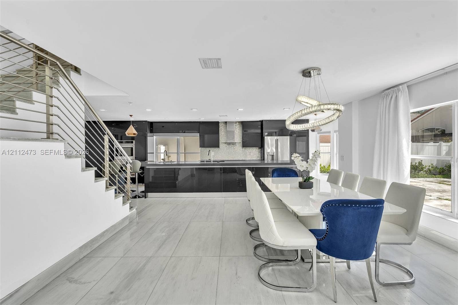 3340 SW 50th Street, Hollywood, Hollywood, FL 33312 Open-concept interior featuring large-format tile flooring, high-gloss cabinetry, stainless steel range hood, stainless steel horizontal railing staircase, and a modern circular LED chandelier