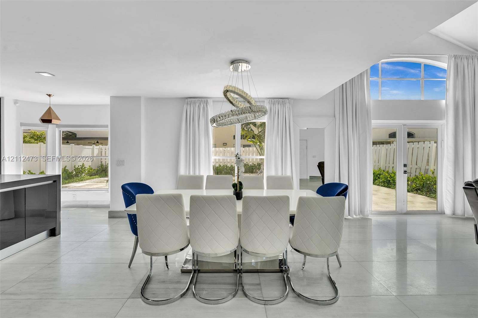 3340 SW 50th Street, Hollywood, Hollywood, FL 33312 Open-concept interior featuring large-format tile flooring, a contemporary multi-ring crystal chandelier, vaulted ceilings, and dual sets of glass-paned doors with arched transom windows
