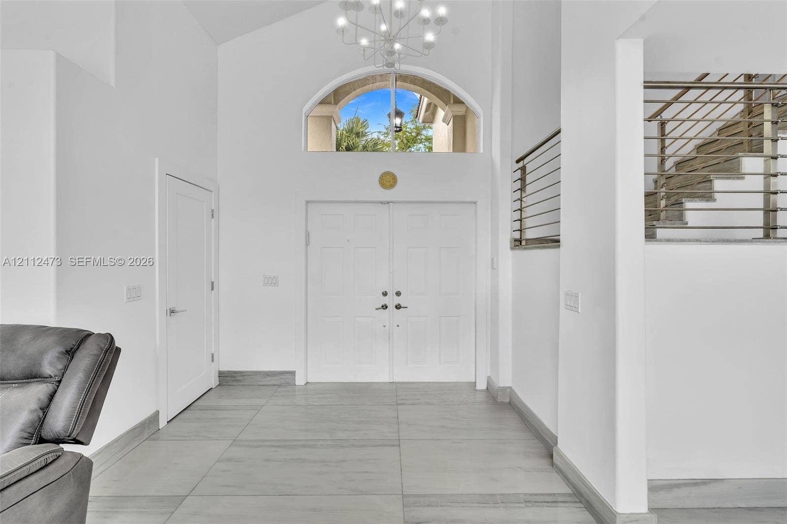 3340 SW 50th Street, Hollywood, Hollywood, FL 33312 Double-door entryway featuring vaulted ceilings, a prominent arched transom window, a contemporary multi-arm chandelier, and metal horizontal-bar railing