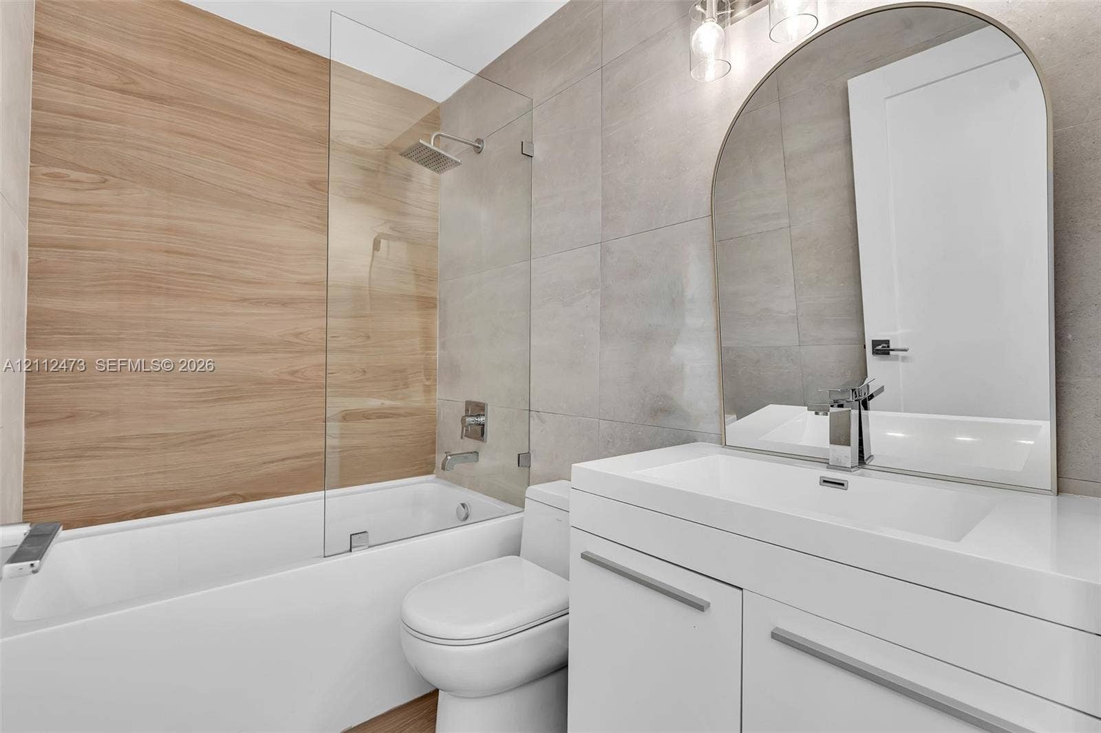 3340 SW 50th Street, Hollywood, Hollywood, FL 33312 Bathroom featuring a floating white vanity with a rectangular sink, arch-top mirror, wood-finish wall tile, frameless glass shower panel, and large-format neutral wall tile