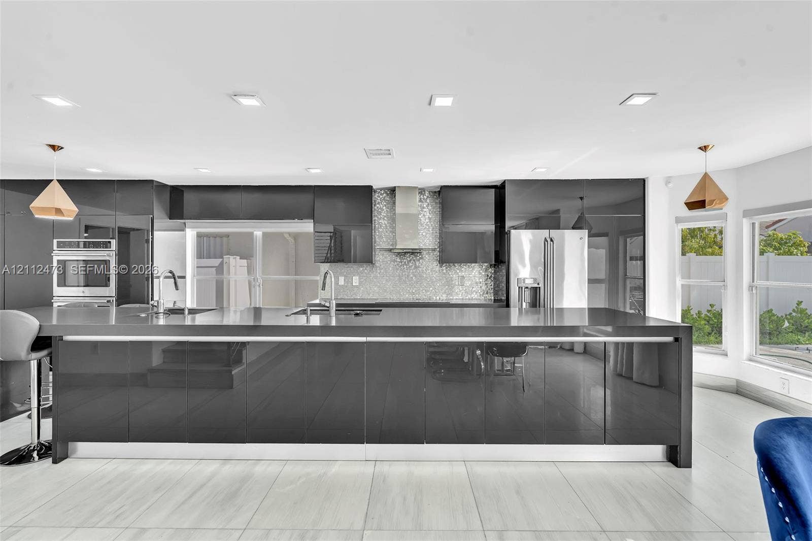 3340 SW 50th Street, Hollywood, Hollywood, FL 33312 Modern kitchen featuring high-gloss cabinetry, a spacious island with a waterfall edge countertop, mosaic tile backsplash, stainless steel appliances, and recessed lighting