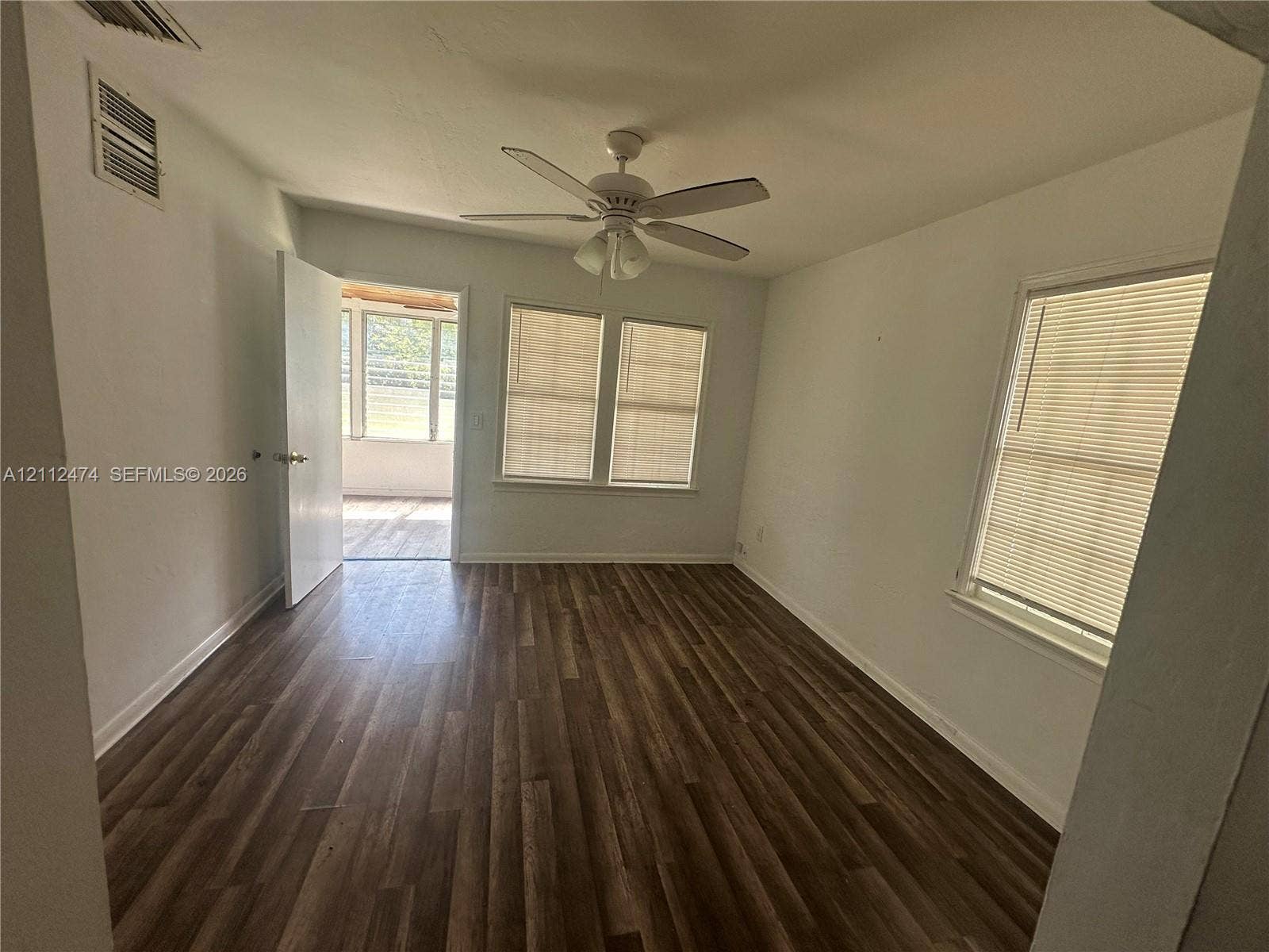 Room featuring wood-finish flooring, a ceiling fan with integrated lighting, and multiple windows with horizontal blinds