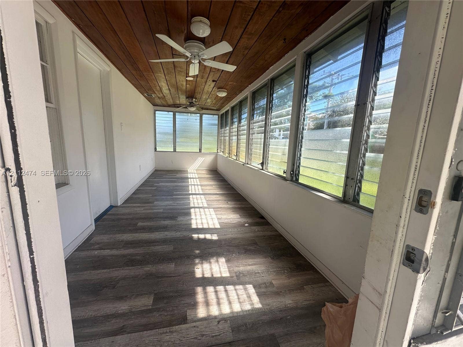 Enclosed porch featuring wood-finish plank flooring, wood-paneled ceiling, adjustable louvered windows, and ceiling-mounted fans