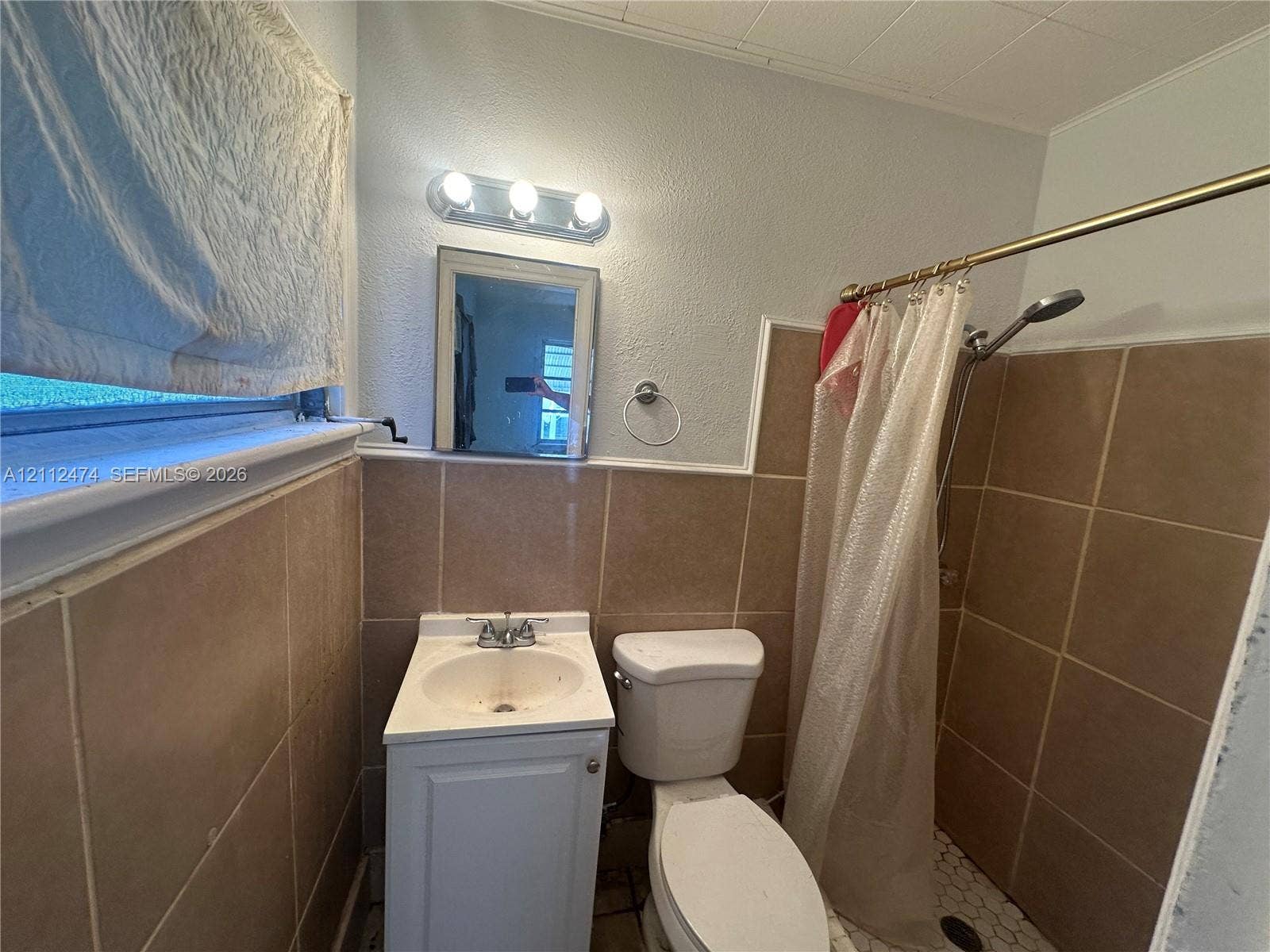 Bathroom featuring neutral-tone square wall tile, pedestal-style vanity with integrated sink, three-light wall-mounted fixture, and a walk-in shower with hexagonal floor tile