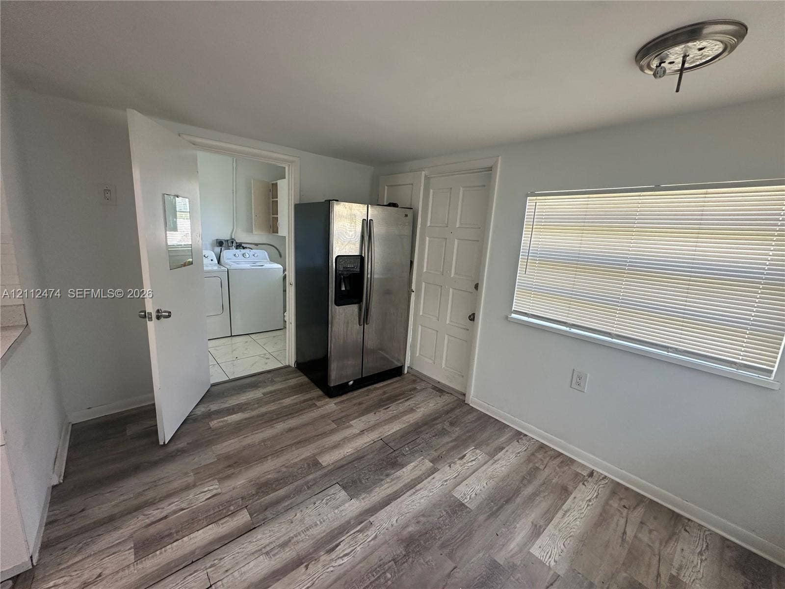 Wood-finish flooring, stainless steel side-by-side refrigerator, multi-panel entry door, and window with horizontal blinds
