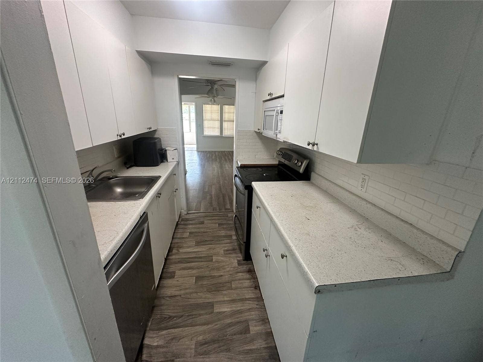 Galley kitchen featuring white cabinetry, light-toned speckled countertops, white subway tile backsplash, wood-finish flooring, and stainless steel appliances