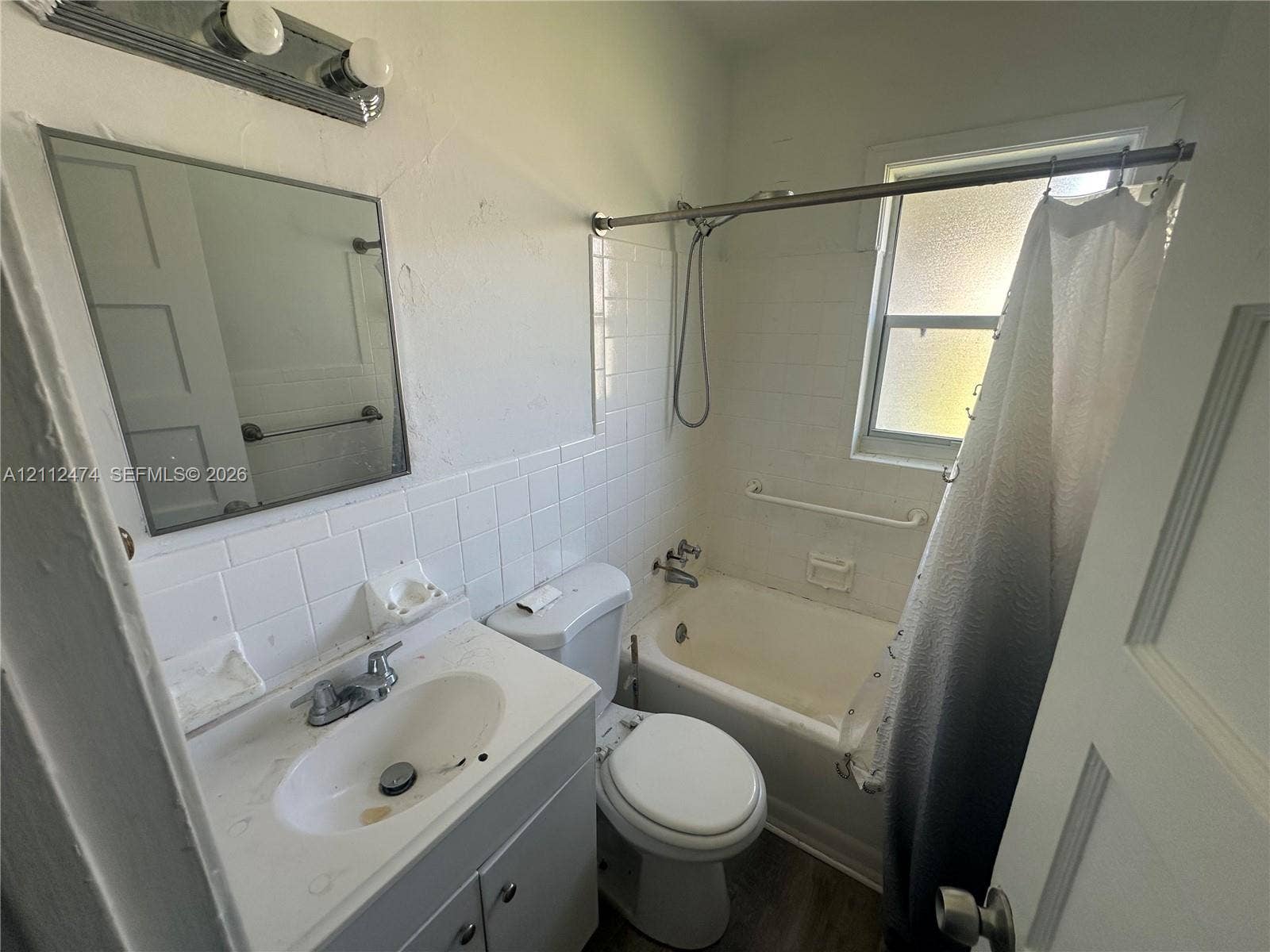 Bathroom featuring a vanity with integrated basin, wall-mounted vanity mirror, white tile shower surround, and a double-light fixture