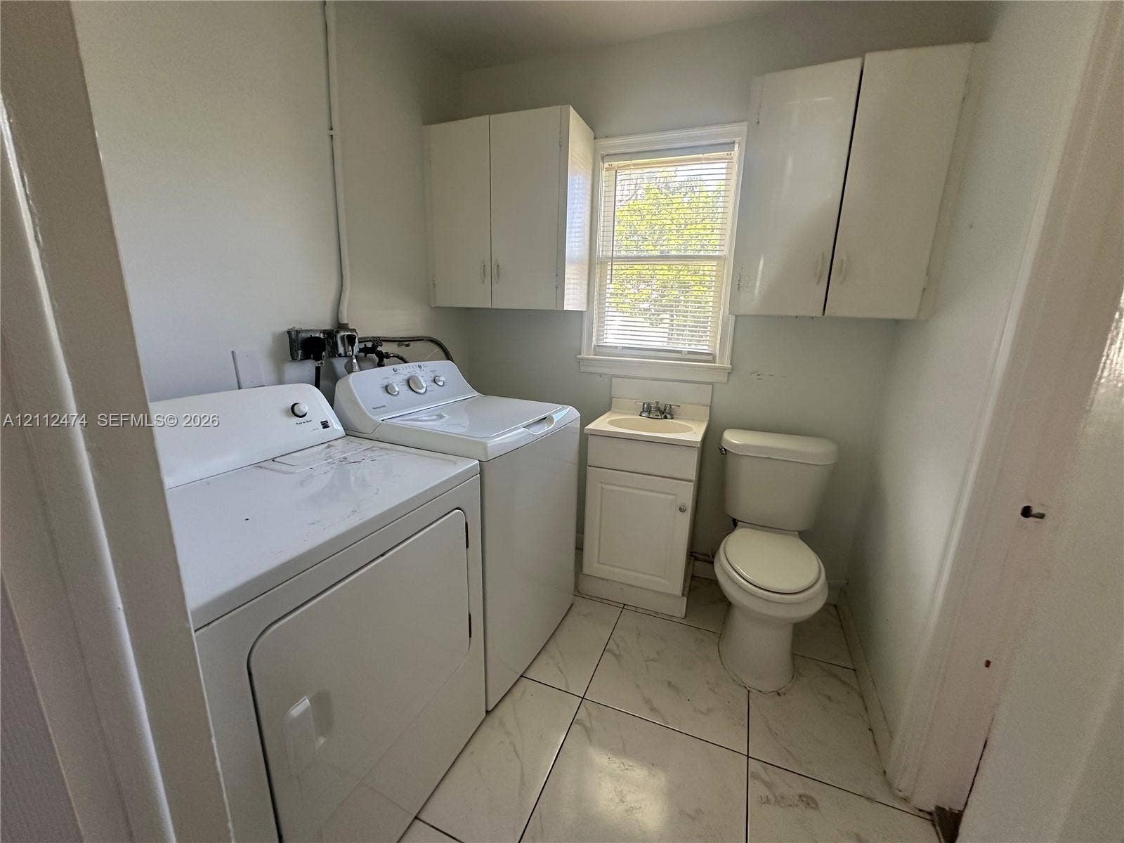 Utility area featuring large-format tile flooring, built-in cabinetry, an integrated sink with storage vanity, and a window with blinds