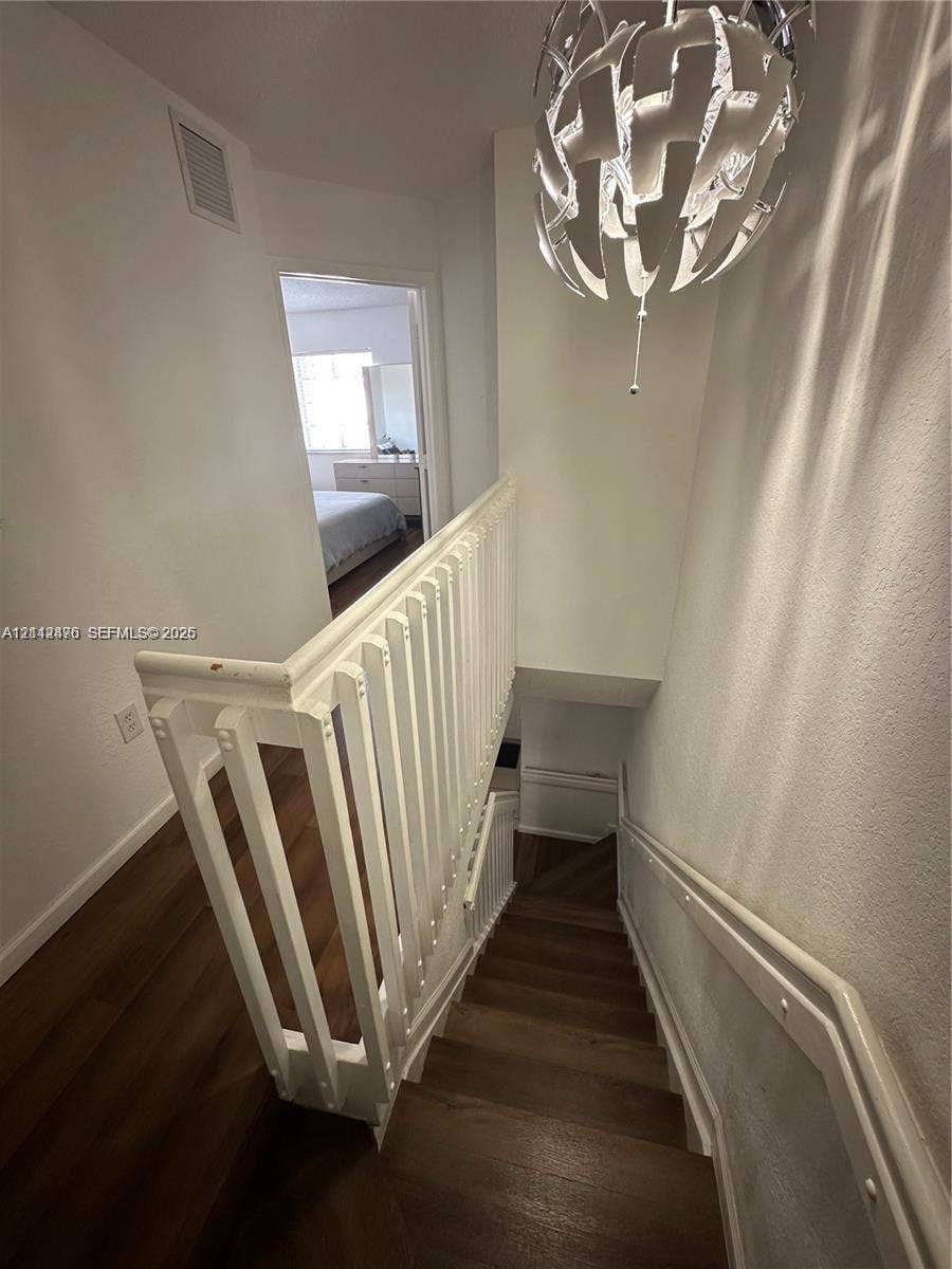 Staircase featuring wood-finish flooring, a white wooden balustrade, and a decorative orb-style pendant light fixture