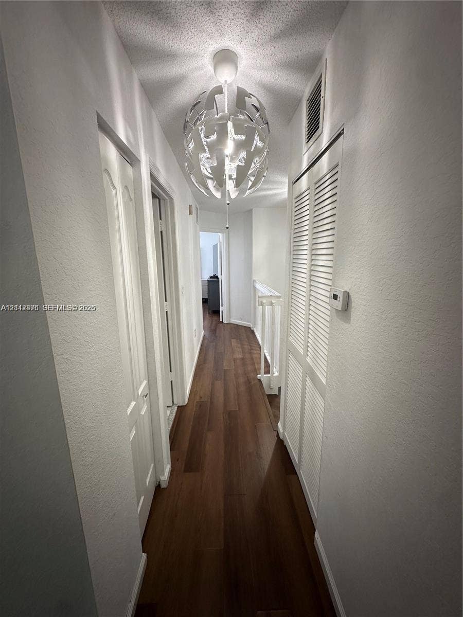 Hallway featuring wood-finish flooring, a geometric spherical pendant light fixture, and double louvered closet doors