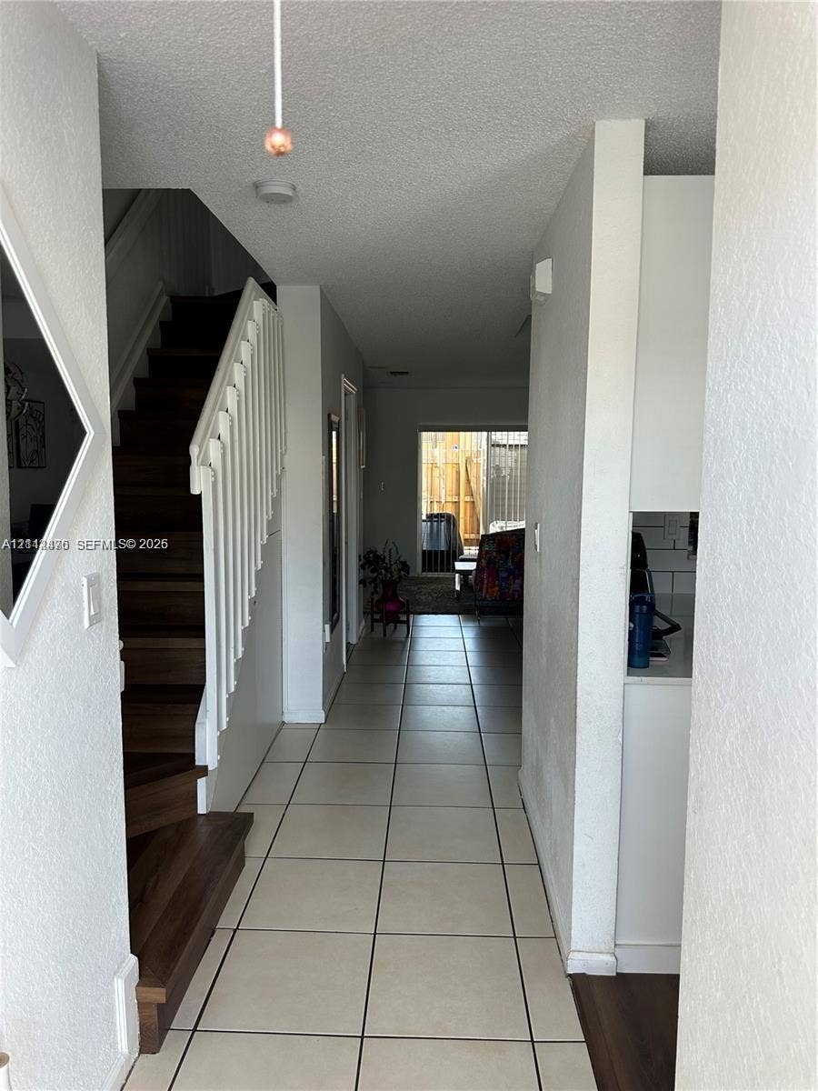 Interior hallway featuring ceramic tile flooring, a staircase with wood-finish treads, and a white balustrade