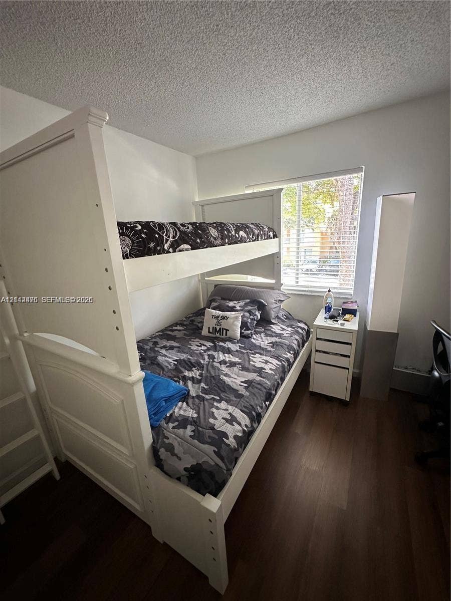 Bedroom featuring dark wood-finish flooring, a neutral wall color palette, and a window with horizontal blinds