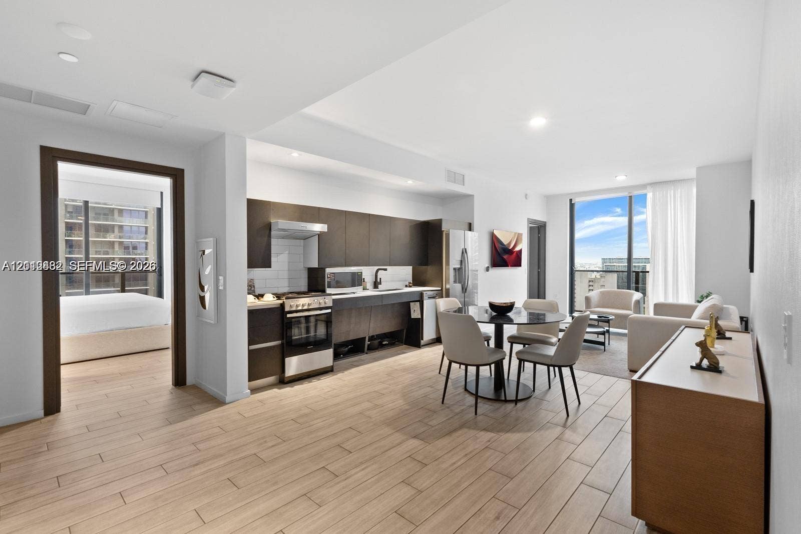 Open-concept interior featuring wood-finish tile flooring, custom flat-panel cabinetry, stainless steel kitchen appliances, and floor-to-ceiling windows
