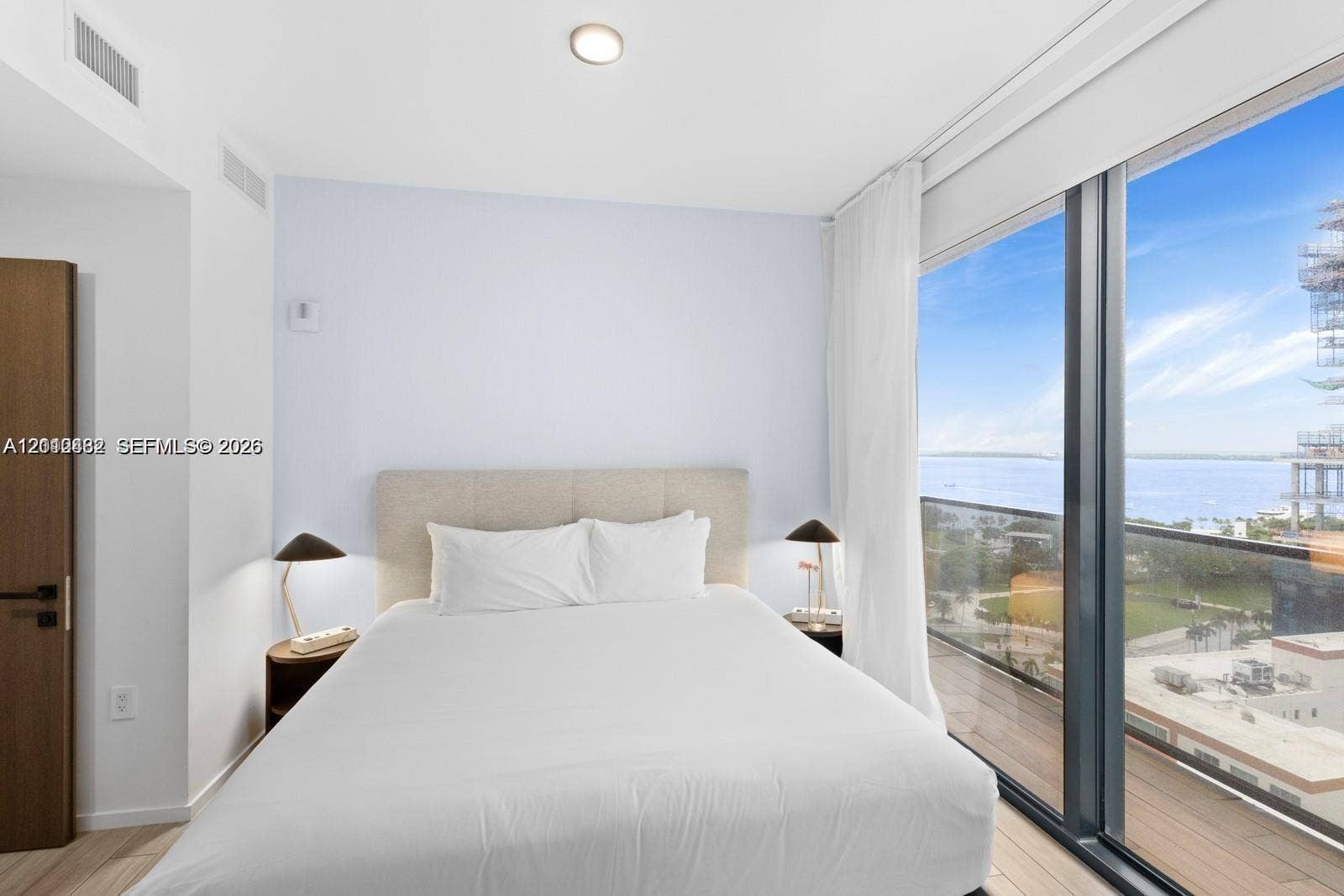 Floor-to-ceiling windows, wood-finish flooring, and access to a private balcony with water scenery