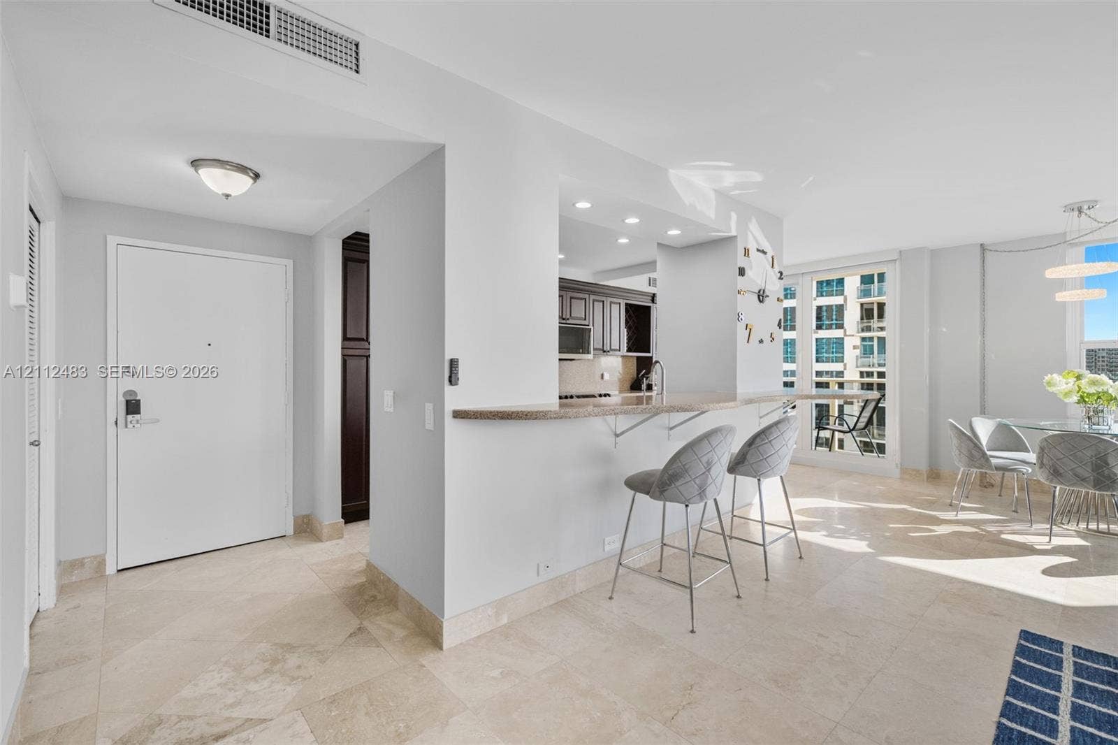 3505 S Ocean Drive, #1101, Hollywood, FL 33019 Open-concept interior featuring stone flooring, a kitchen pass-through counter, recessed lighting, and a glass-paneled door leading to an exterior balcony