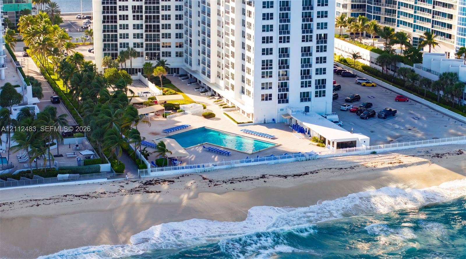 3505 S Ocean Drive, #1101, Hollywood, FL 33019 High-rise residential building featuring direct beach access, an L-shaped swimming pool, paved surface parking, and mature palm landscaping