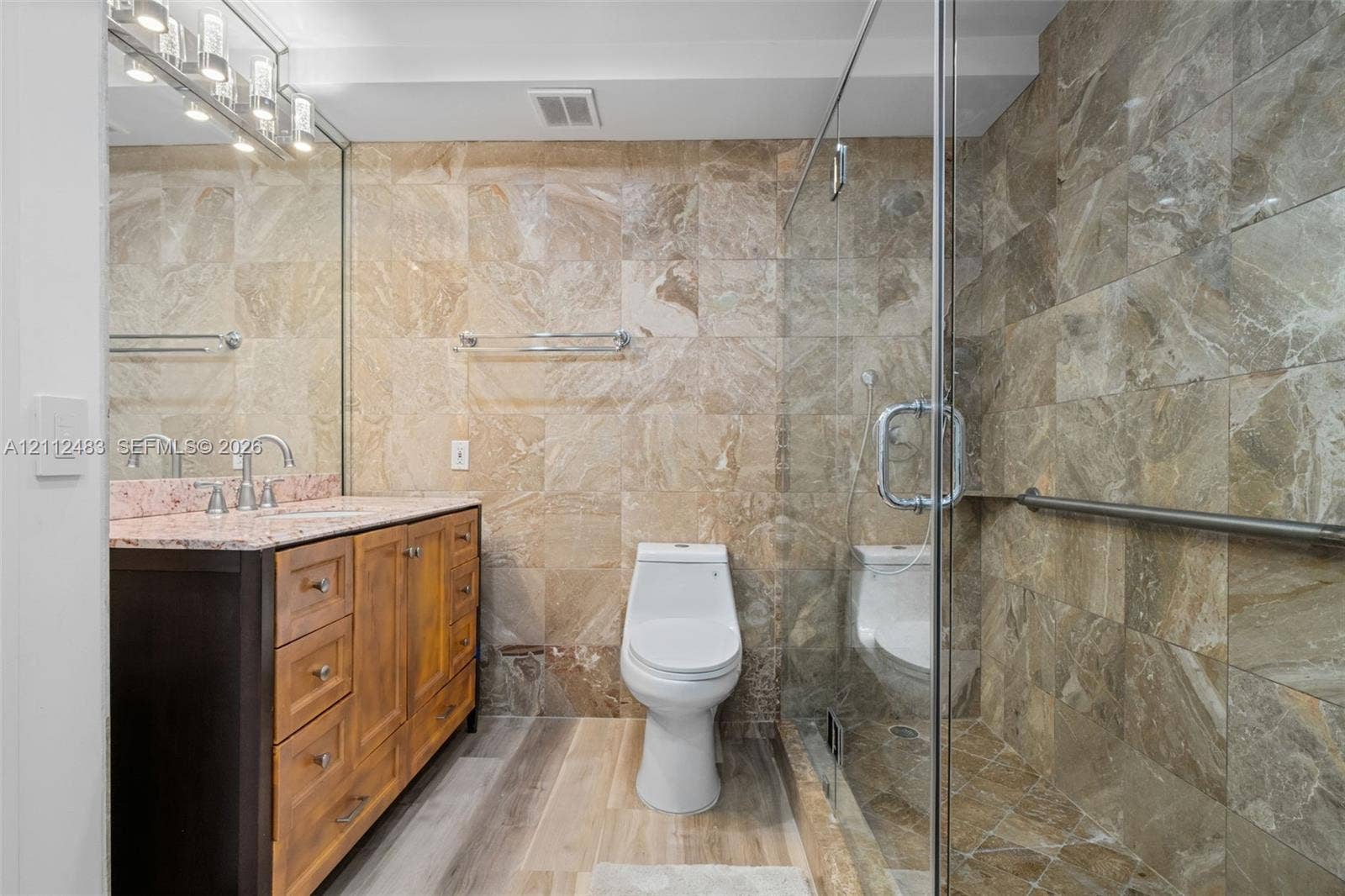 3505 S Ocean Drive, #1101, Hollywood, FL 33019 Bathroom featuring stone-tile wall finishes, wood-finish cabinetry with a stone countertop, a glass-enclosed shower, and a polished-chrome light fixture