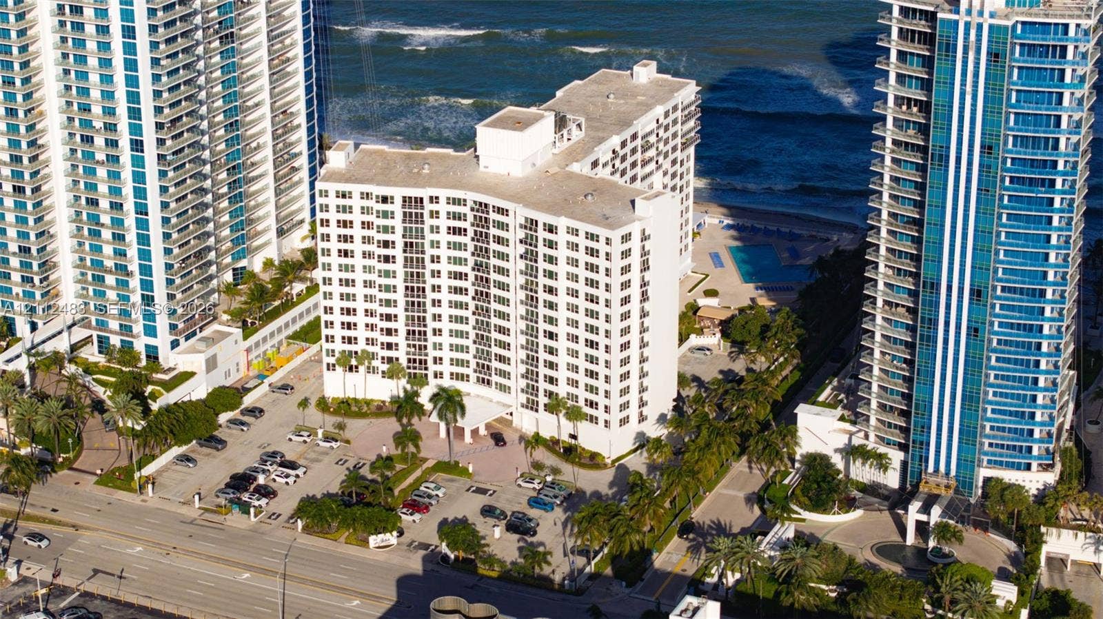 3505 S Ocean Drive, #1101, Hollywood, FL 33019 Aerial perspective of high-rise building featuring proximity to the coastline, paved surface parking, mature palm trees, and an outdoor swimming pool