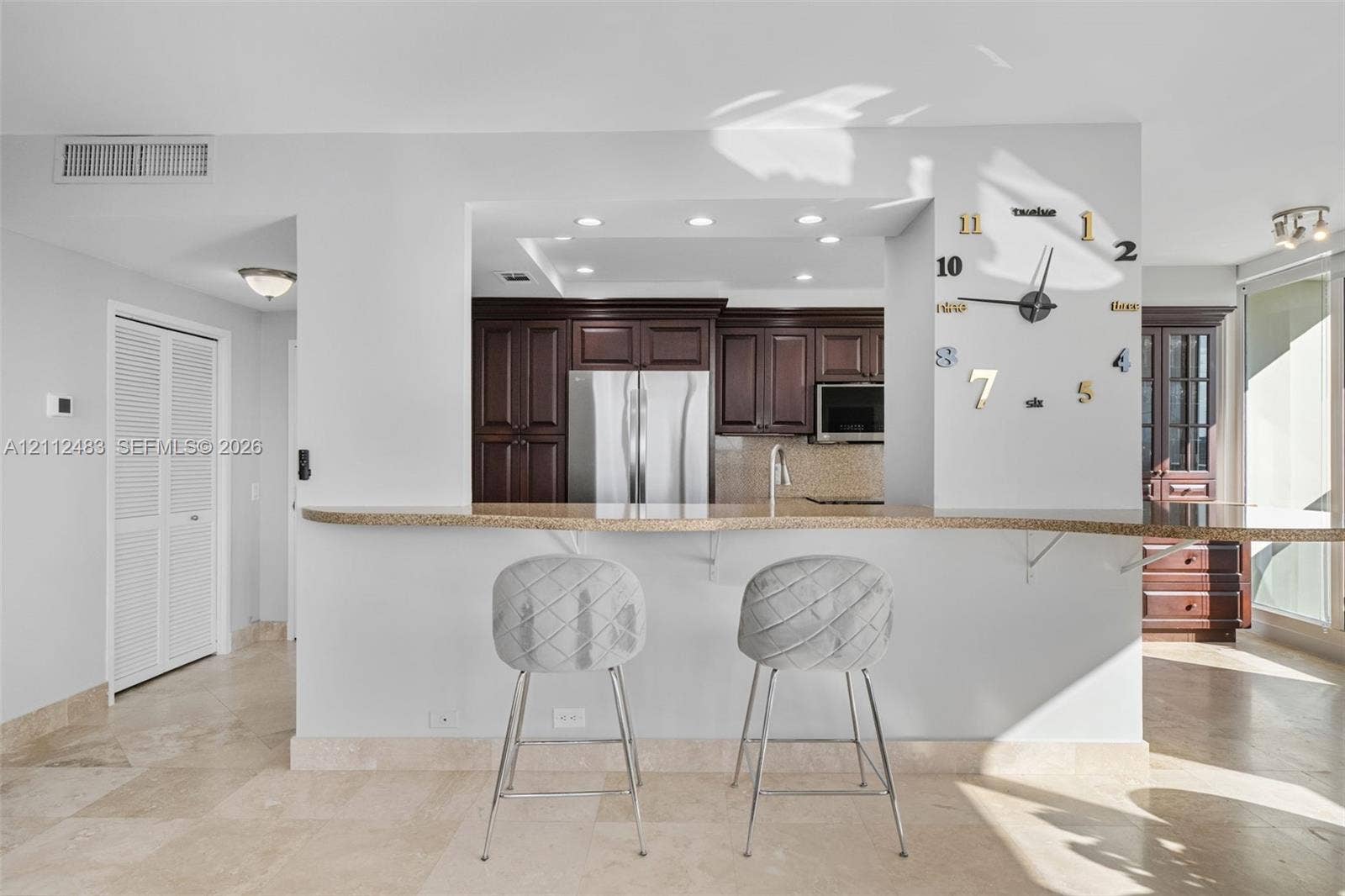 3505 S Ocean Drive, #1101, Hollywood, FL 33019 Kitchen pass-through window featuring a stone-topped breakfast bar, dark wood cabinetry, stainless steel appliances, recessed ceiling lighting, and tile flooring