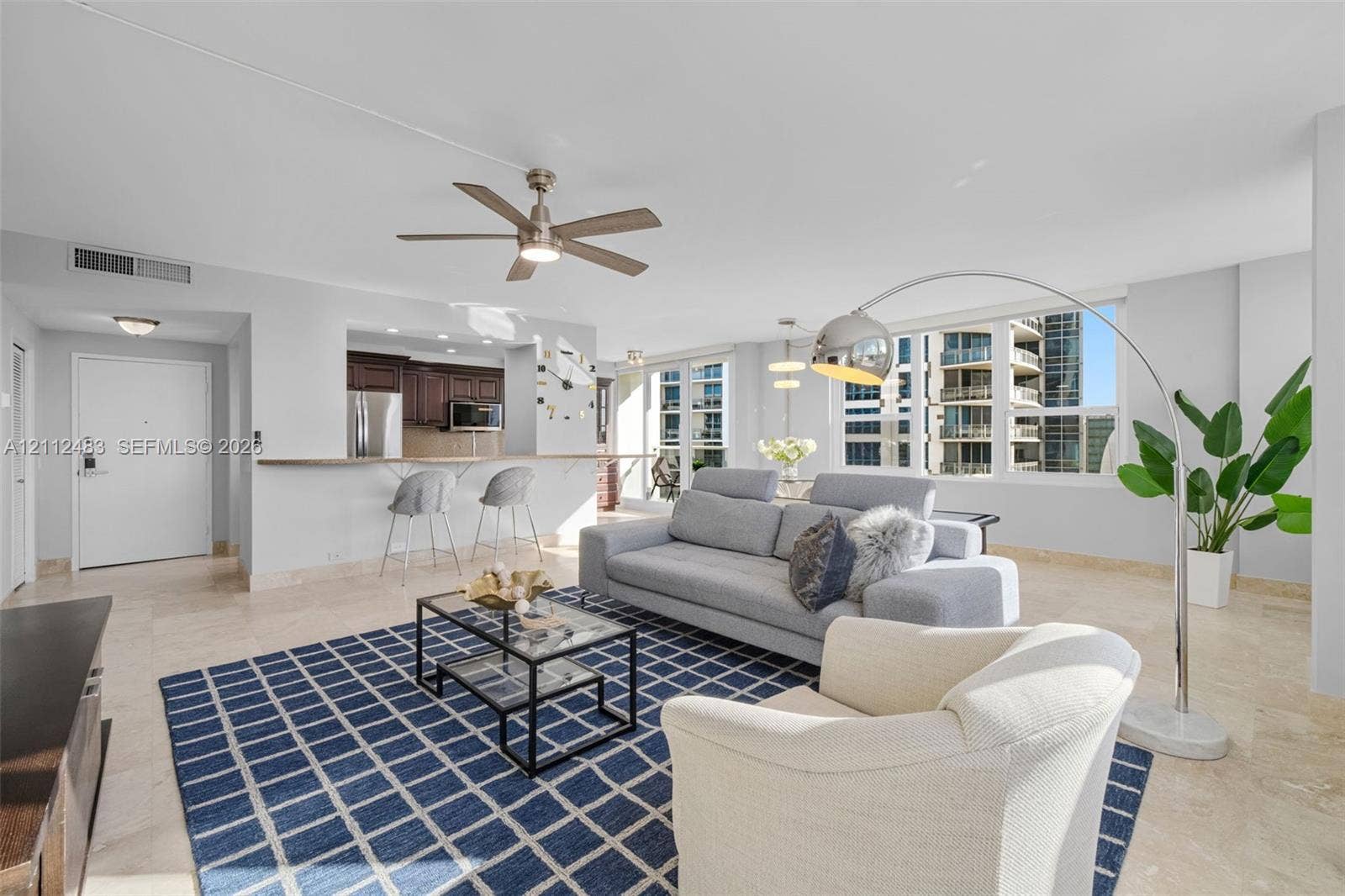 3505 S Ocean Drive, #1101, Hollywood, FL 33019 Open-concept living space featuring natural stone flooring, large windows, dark wood-finish cabinetry, a breakfast bar, and a ceiling fan with integrated lighting