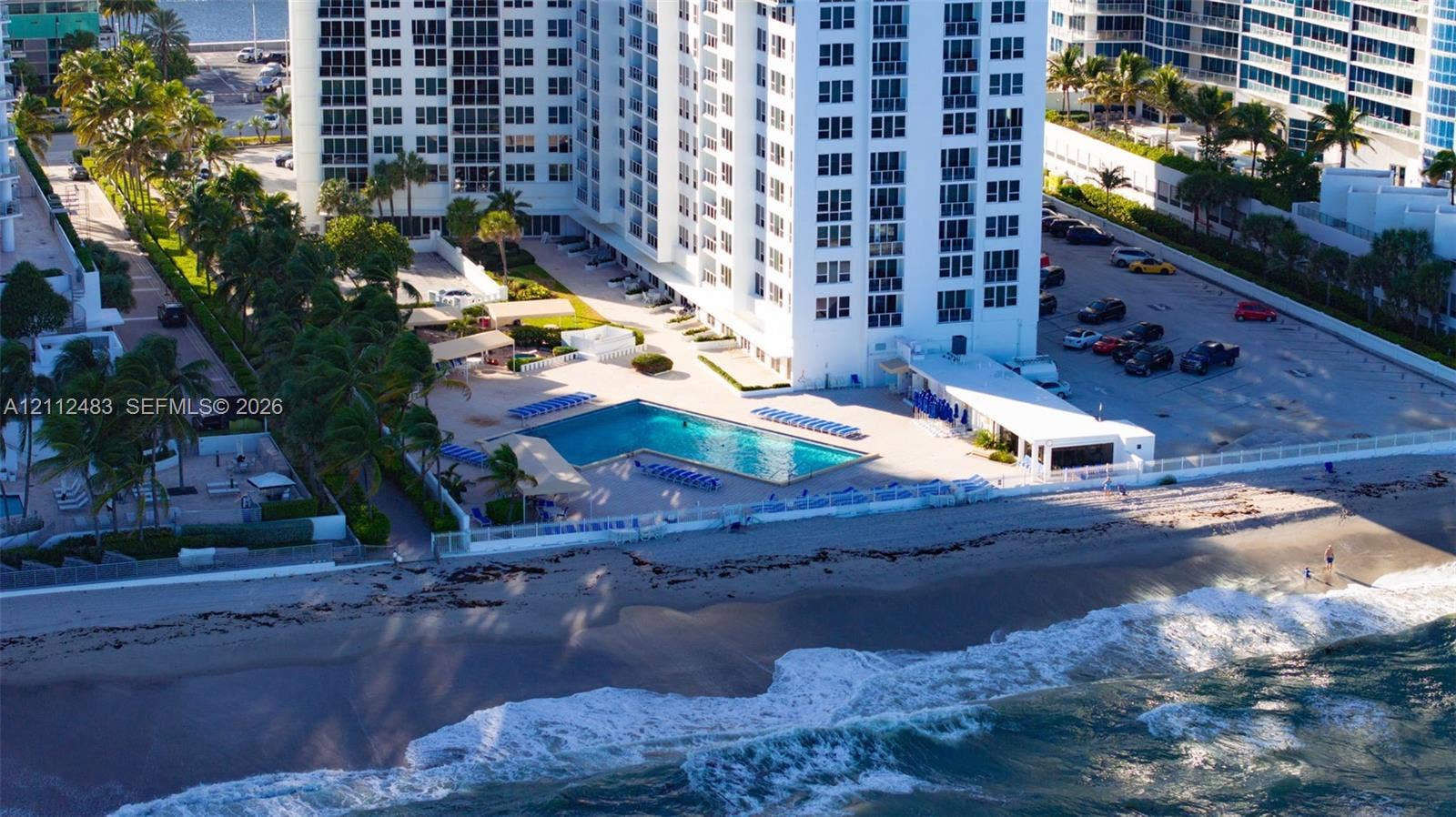 3505 S Ocean Drive, #1101, Hollywood, FL 33019 High-rise residential building featuring a waterfront swimming pool, paved sundeck, landscaped grounds with palm trees, and direct oceanfront access