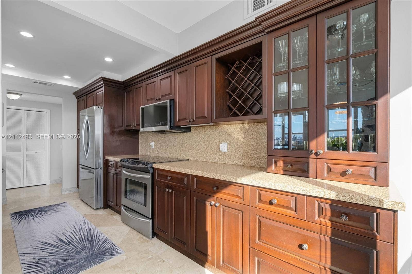 3505 S Ocean Drive, #1101, Hollywood, FL 33019 Kitchen featuring cherry-finish cabinetry, stone-texture countertops, stainless steel appliances, built-in wine storage, and glass-paneled display cabinets