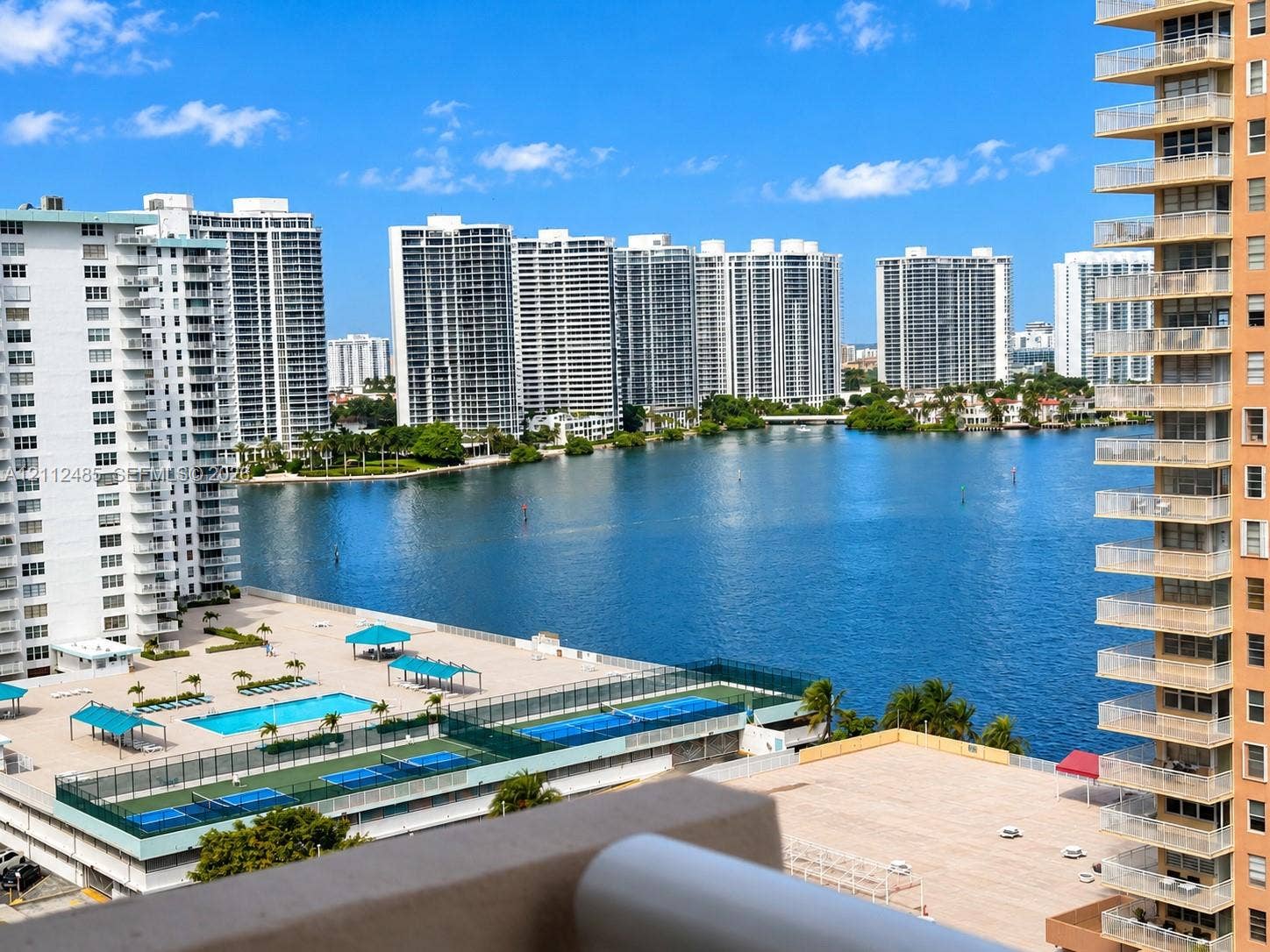 250 174th Street, #1707, Sunny Isles Beach, Sunny Isles Beach, FL 33160 Elevated balcony overview featuring an outdoor swimming pool, fenced tennis courts, and expansive water frontage