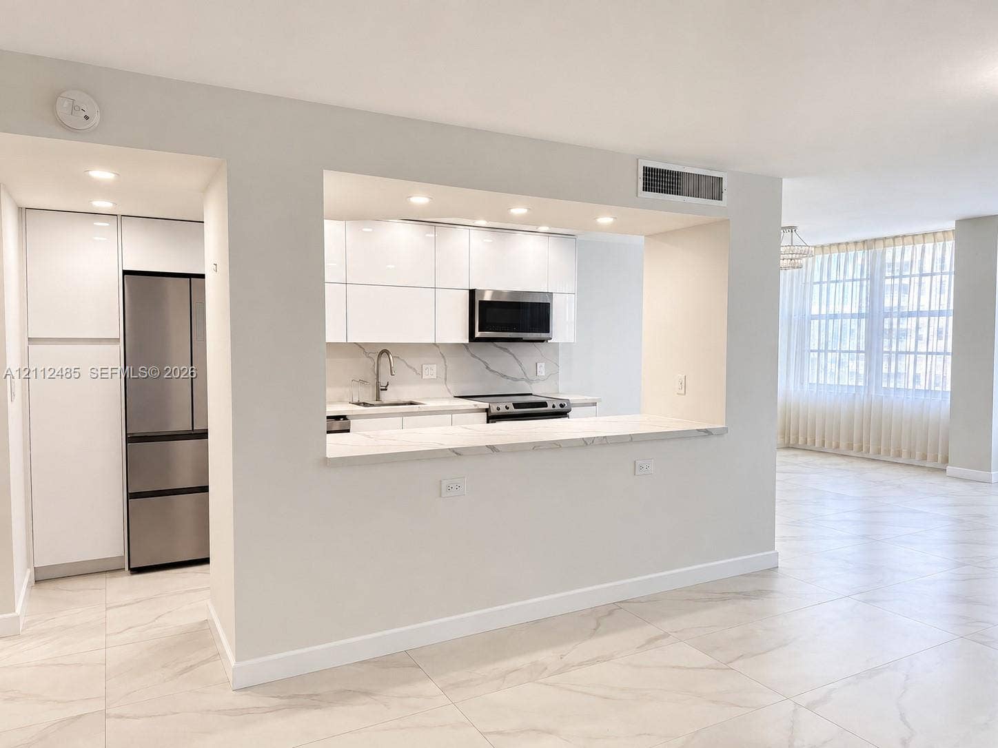 250 174th Street, #1707, Sunny Isles Beach, Sunny Isles Beach, FL 33160 Kitchen featuring high-gloss white cabinetry, stone-finish countertops with waterfall edge, stainless steel refrigerator, built-in microwave, and large-format tile flooring
