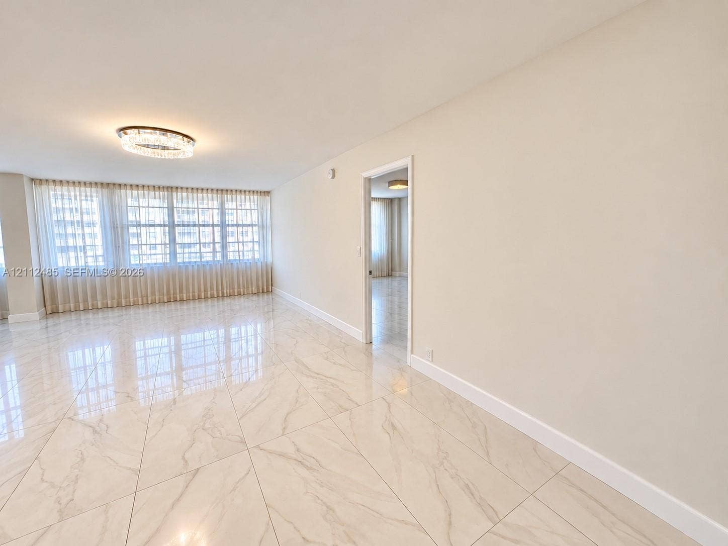 250 174th Street, #1707, Sunny Isles Beach, Sunny Isles Beach, FL 33160 Large-format polished flooring with veined detailing, floor-to-ceiling windows with integrated drapery, and a contemporary circular flush-mount light fixture