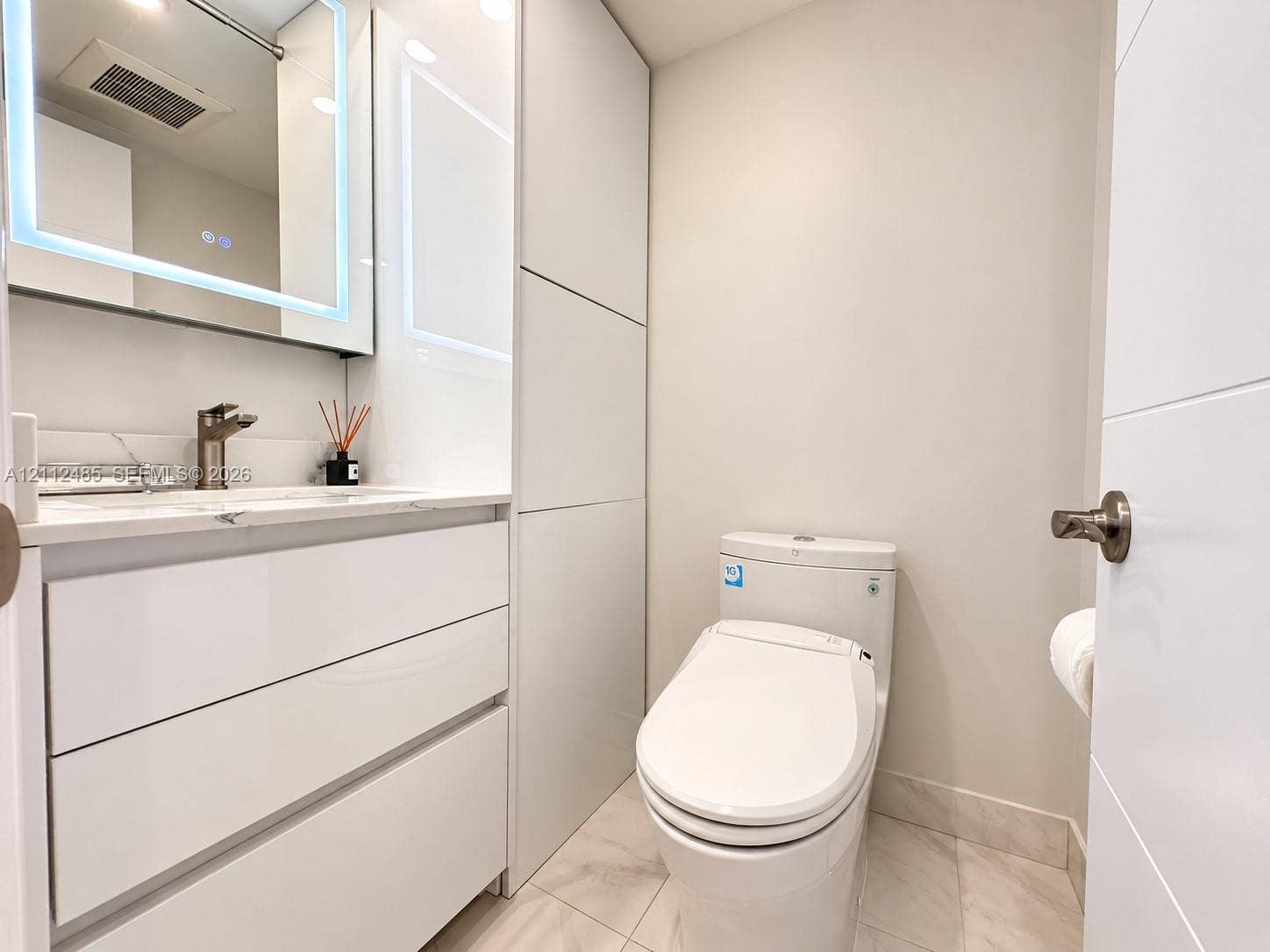 250 174th Street, #1707, Sunny Isles Beach, Sunny Isles Beach, FL 33160 Modern vanity with integrated storage, stone-surfaced countertop, LED-backlit mirror, and neutral tile flooring
