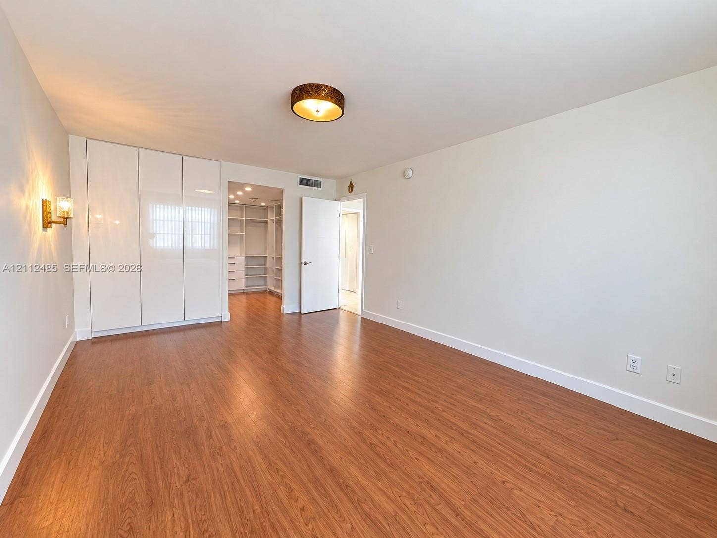 250 174th Street, #1707, Sunny Isles Beach, Sunny Isles Beach, FL 33160 Wood-finish flooring, full-height white cabinetry with smooth-finish doors, built-in closet shelving system, brass-tone wall-mounted lighting, and a drum-style ceiling light fixture
