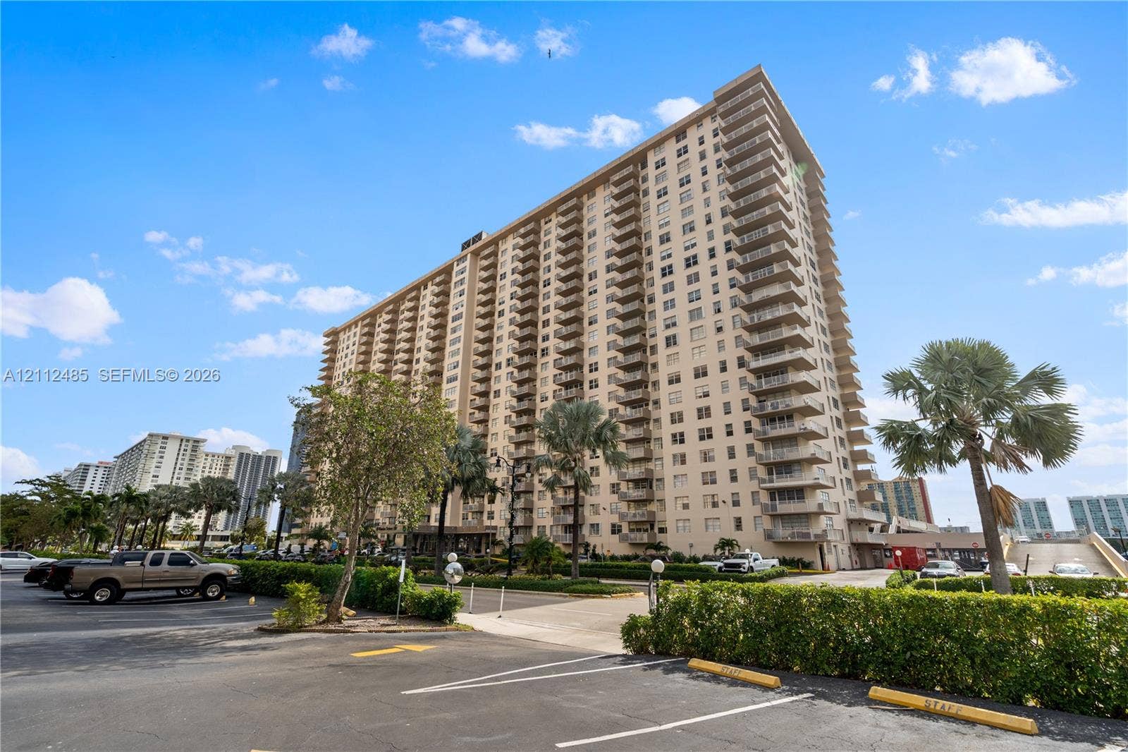 250 174th Street, #1707, Sunny Isles Beach, Sunny Isles Beach, FL 33160 High-rise residential exterior featuring expansive concrete balconies, structured architectural facade, and paved parking area with established landscape greenery