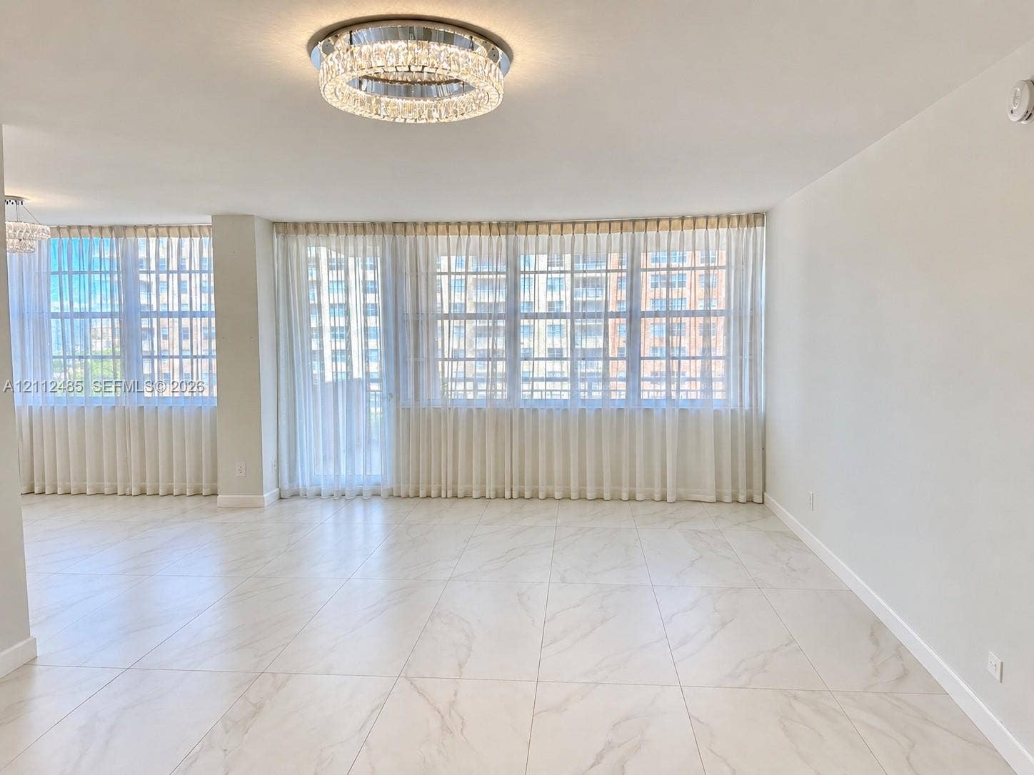 250 174th Street, #1707, Sunny Isles Beach, Sunny Isles Beach, FL 33160 Open-concept interior featuring large-format tile flooring with marble-style veining, floor-to-ceiling windows, and a tiered crystal flush-mount ceiling fixture