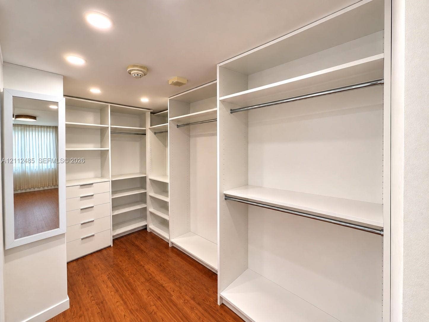 250 174th Street, #1707, Sunny Isles Beach, Sunny Isles Beach, FL 33160 Custom walk-in closet featuring white built-in shelving, integrated dresser drawers, metal hanging rods, and wood-finish flooring