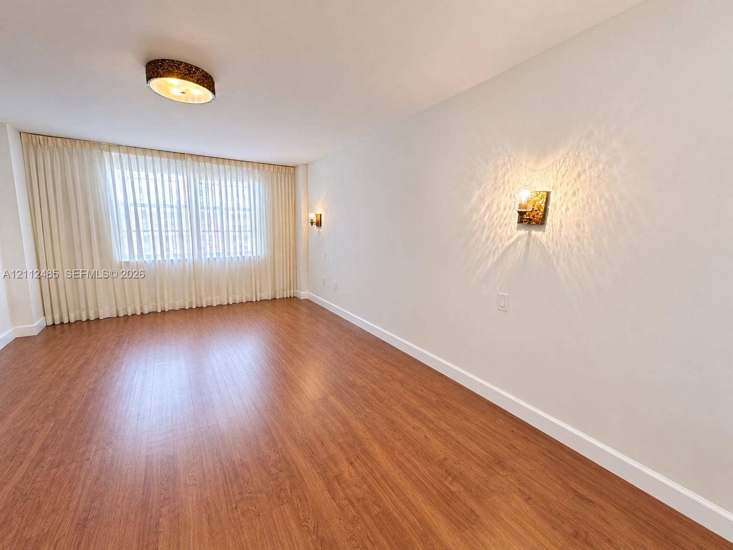250 174th Street, #1707, Sunny Isles Beach, Sunny Isles Beach, FL 33160 Neutral interior featuring wood-finish flooring, a drum-style ceiling fixture, wall-mounted decorative sconces, and full-length window treatments